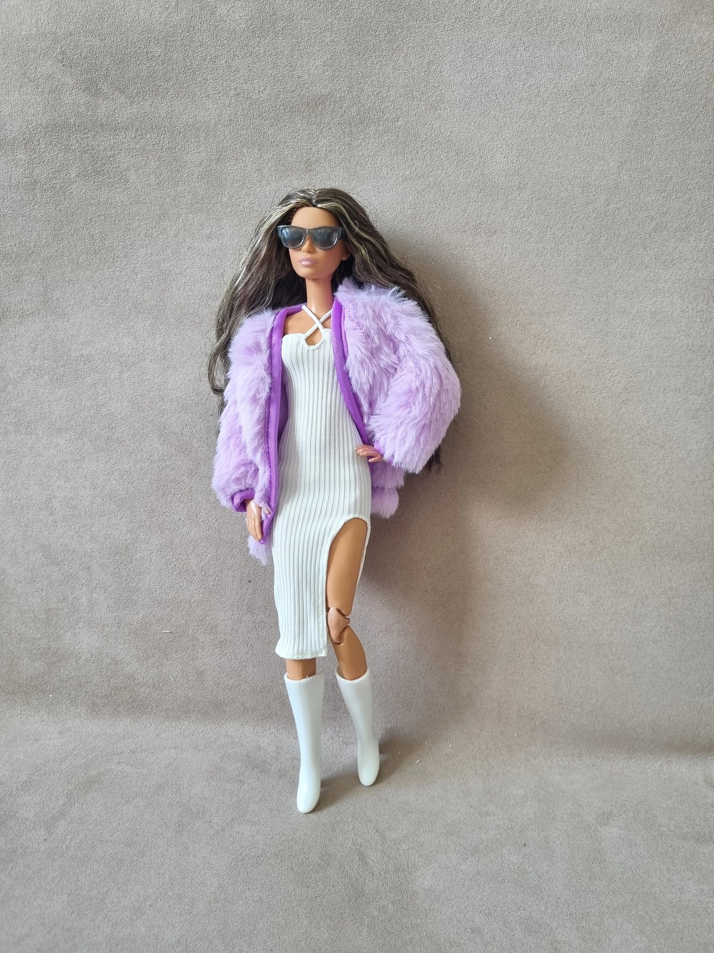 Fashion doll models glamorous look: white ribbed dress with slit, lavender faux fur coat, sunglasses, and white boots.