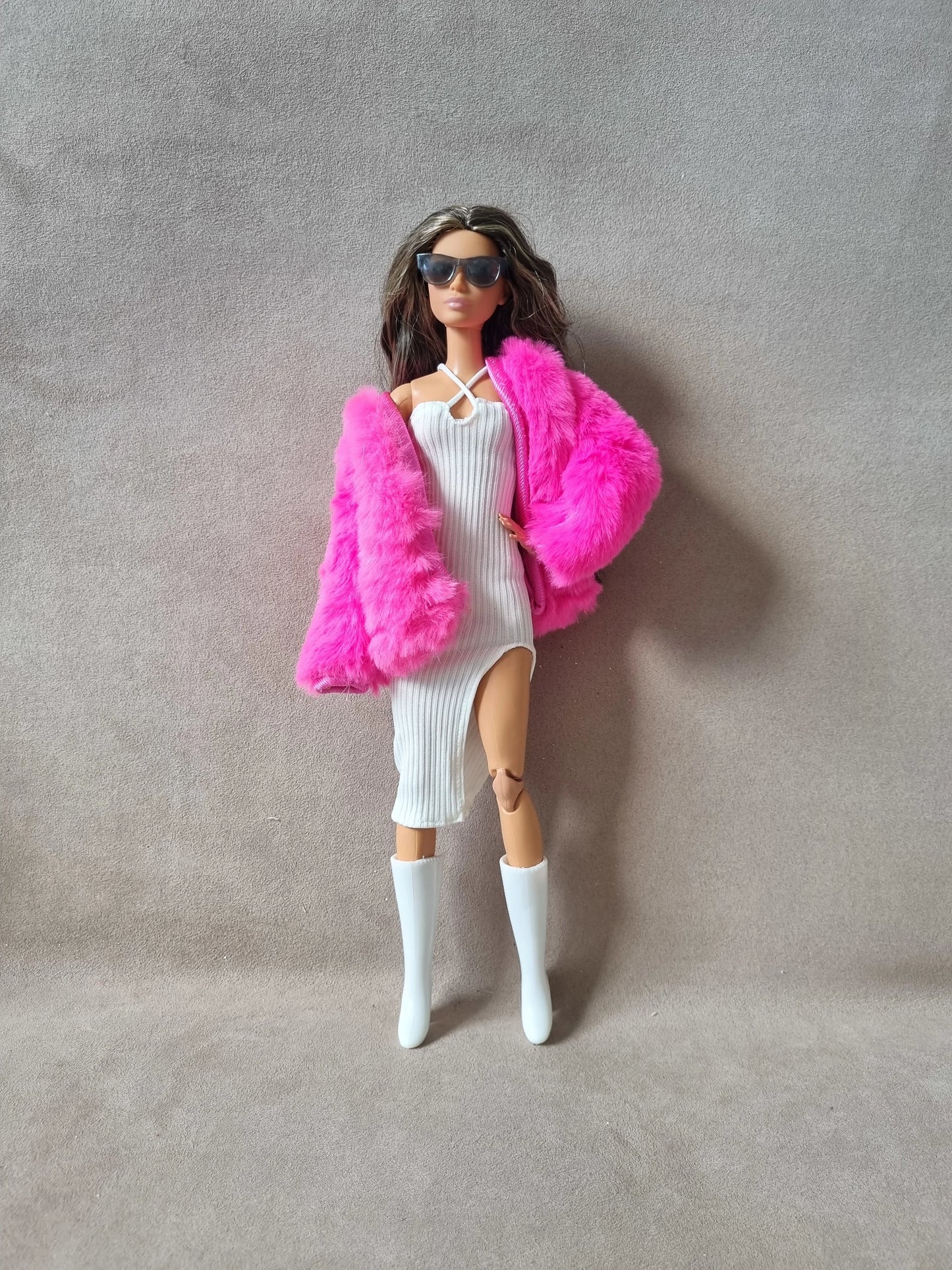 Full outfit view of Barbie doll in white ribbed dress, hot pink faux fur coat, sunglasses, and white boots.