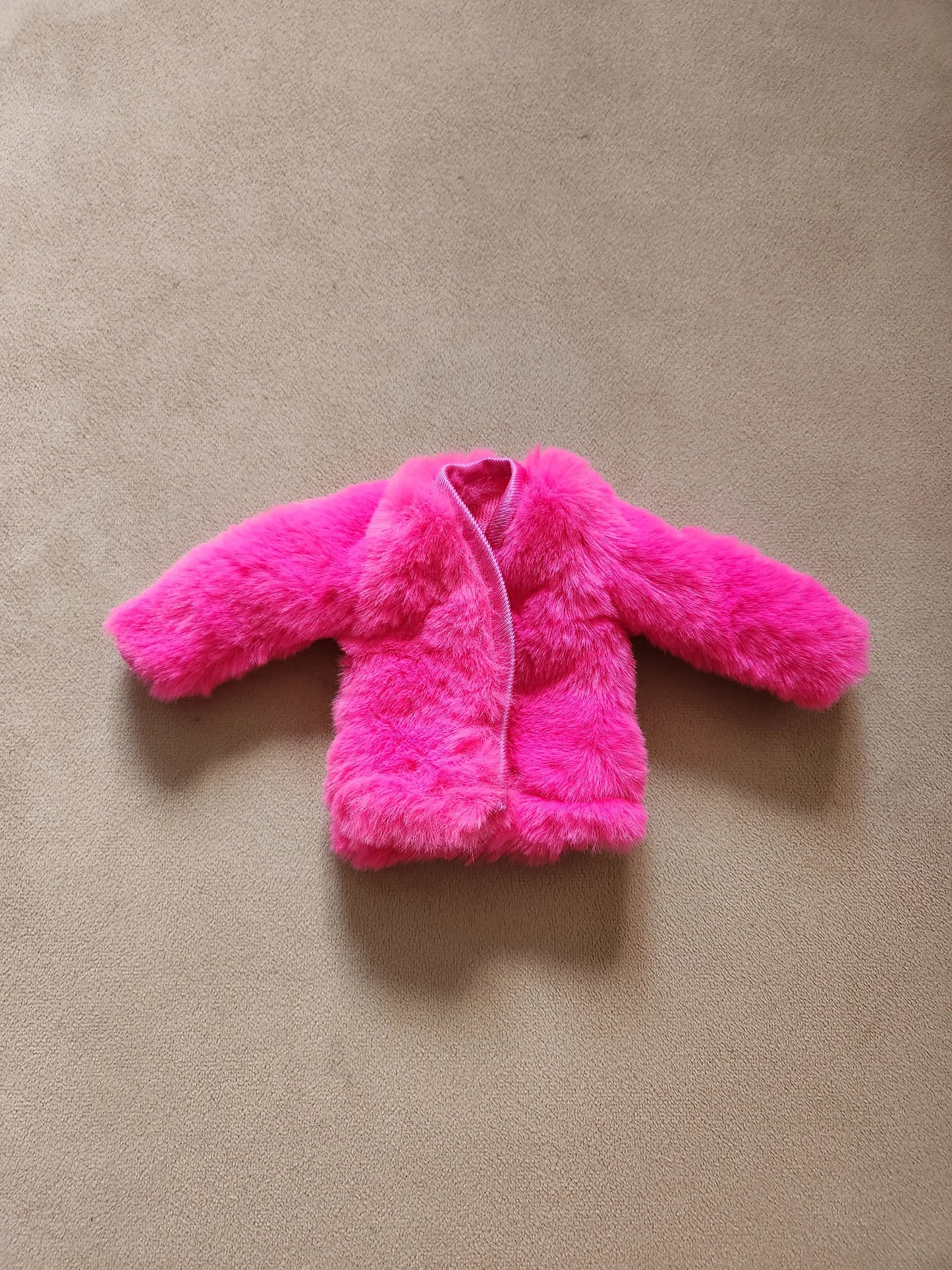 Hot pink faux fur open-front coat for Barbie doll, laid flat on beige background.
