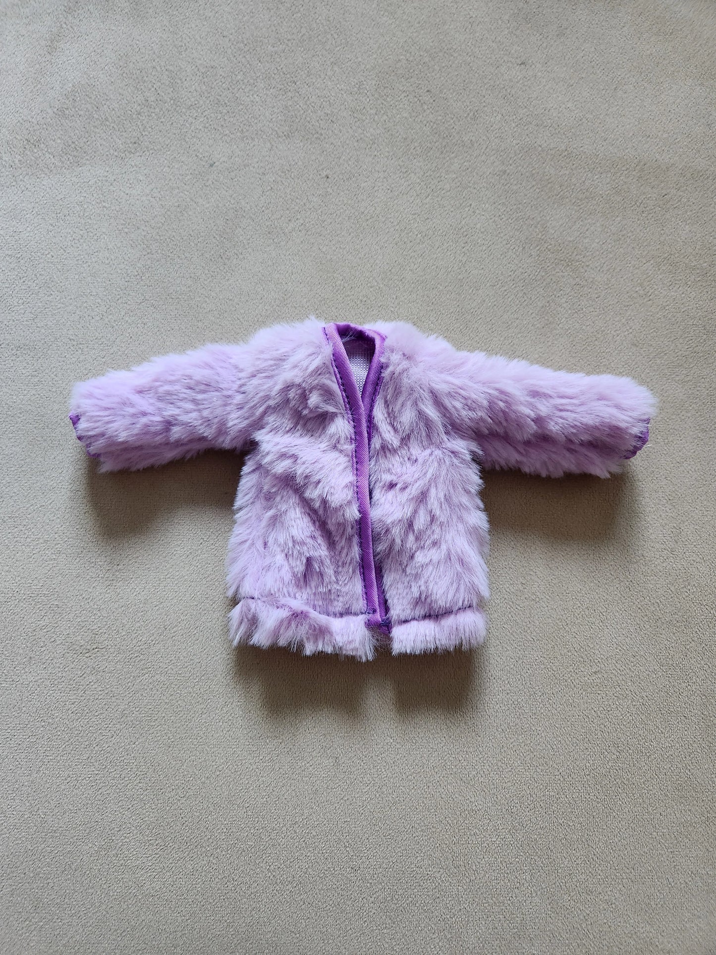 Soft lavender purple faux fur open-front coat for Barbie doll, laid flat on beige background.