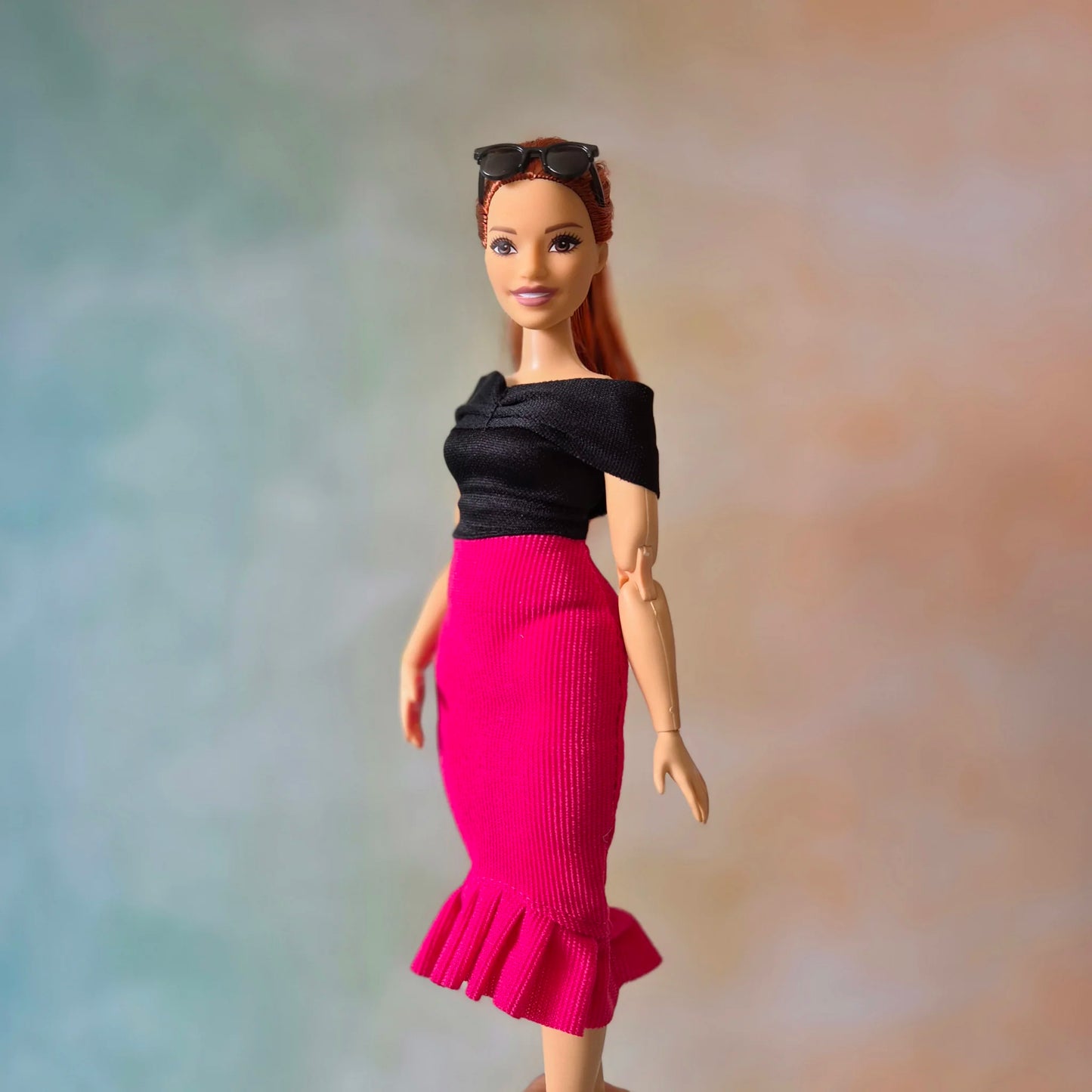 Profile view of Barbie doll in chic black top and vibrant pink textured mermaid skirt.