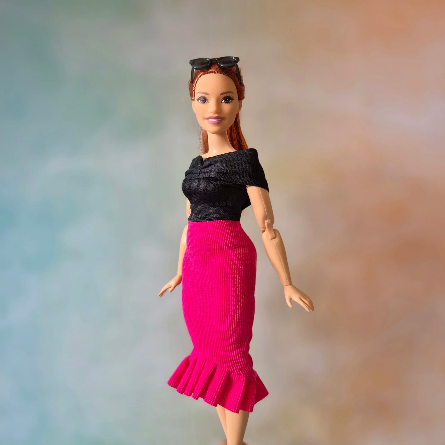 Full body shot of Barbie doll in black top, hot pink mermaid skirt, and black pointed shoes.