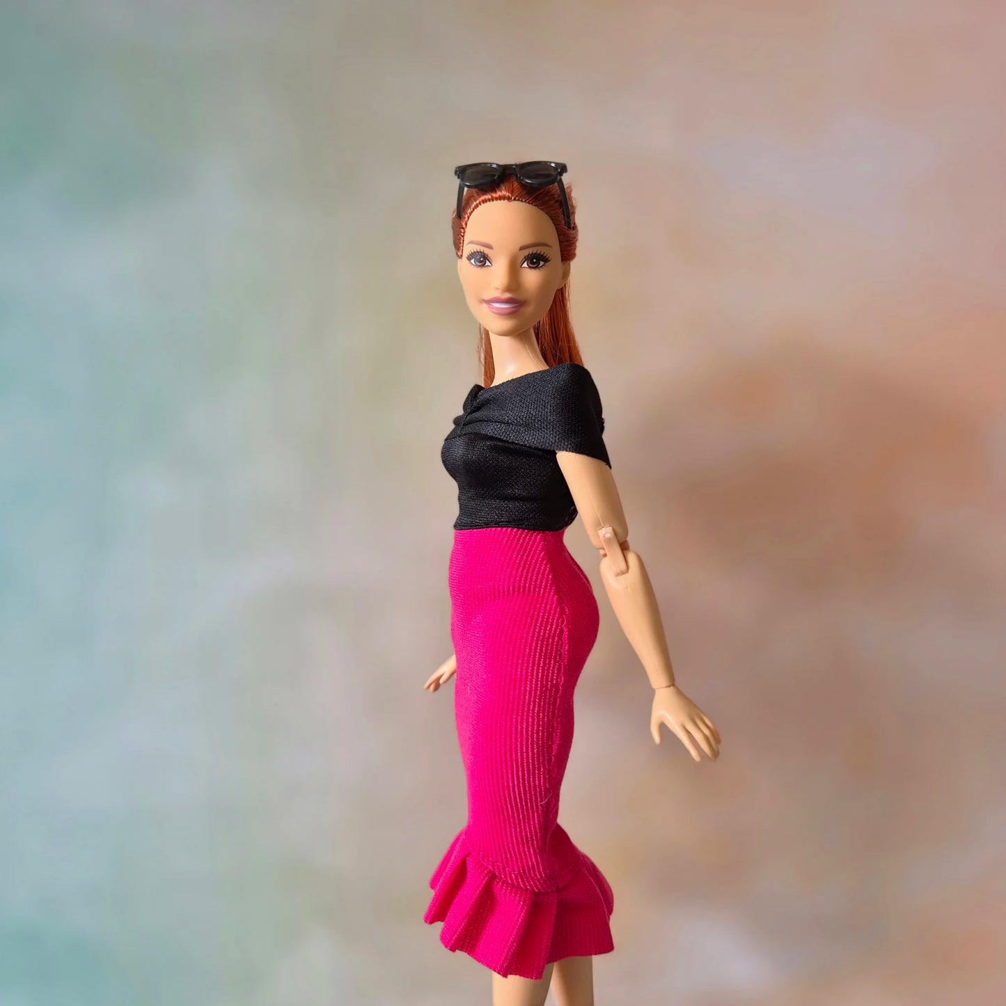 Stylish Barbie doll with red hair in black off-shoulder top and hot pink ruffle hem skirt.