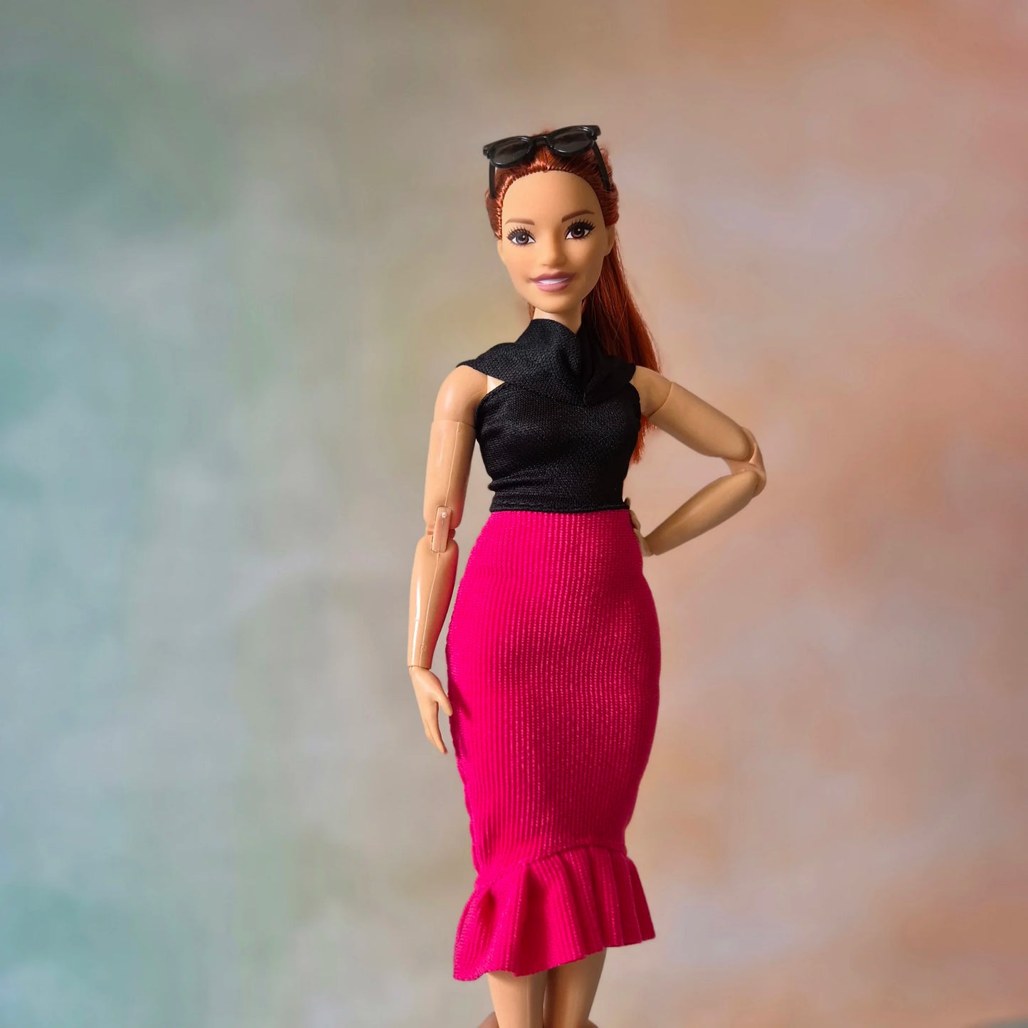 Red-haired Barbie doll posing confidently in black cowl neck top and hot pink mermaid skirt.