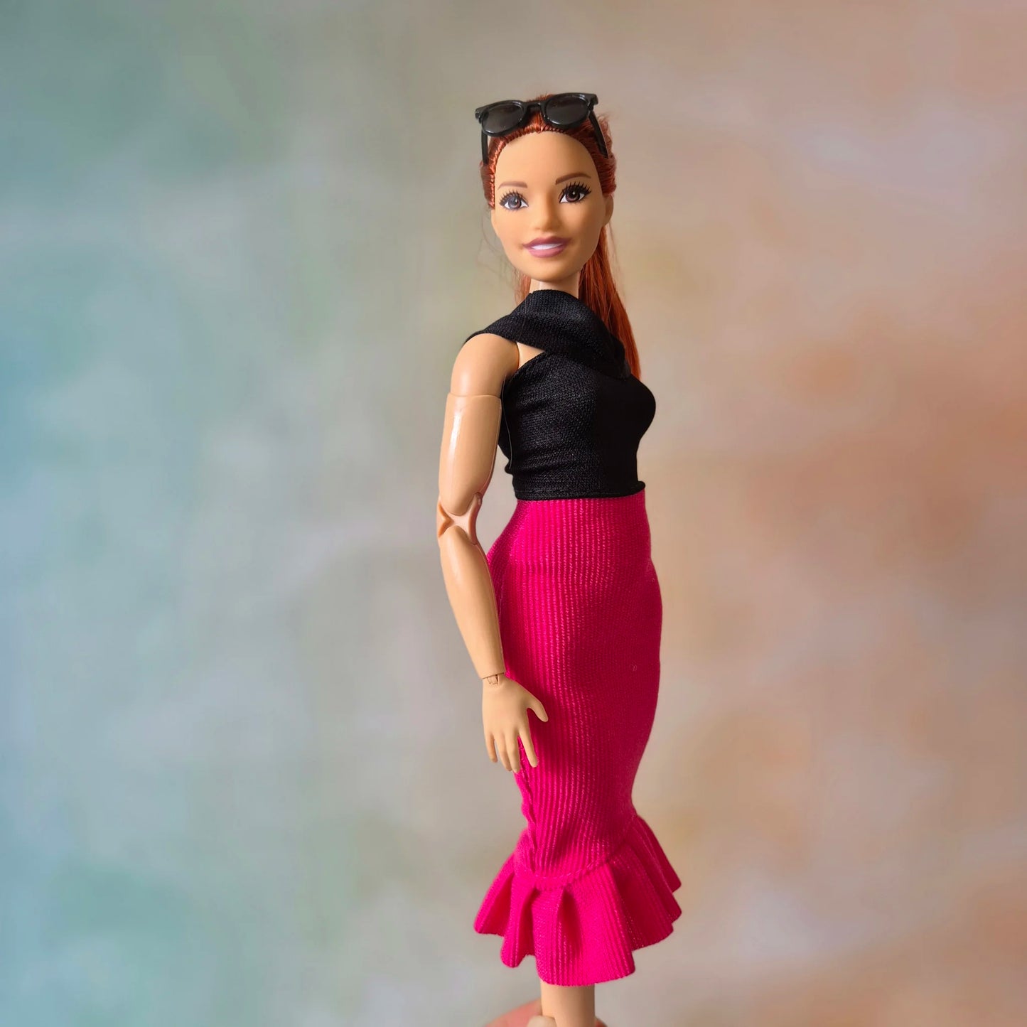 Barbie doll looking over shoulder, showcasing black top and hot pink ruffle mermaid skirt.