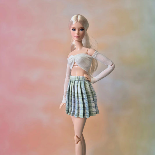 Barbie doll with platinum blonde hair in white mesh sleeve crop top and light green plaid skirt.