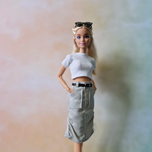 Barbie doll wearing a white crop top and khaki skirt with a black belt.