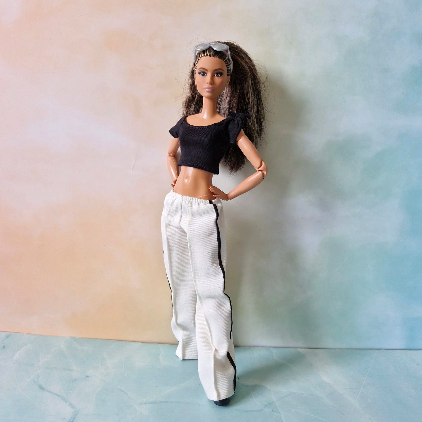 Barbie doll stands confidently in black crop top and white striped pants fashion set.