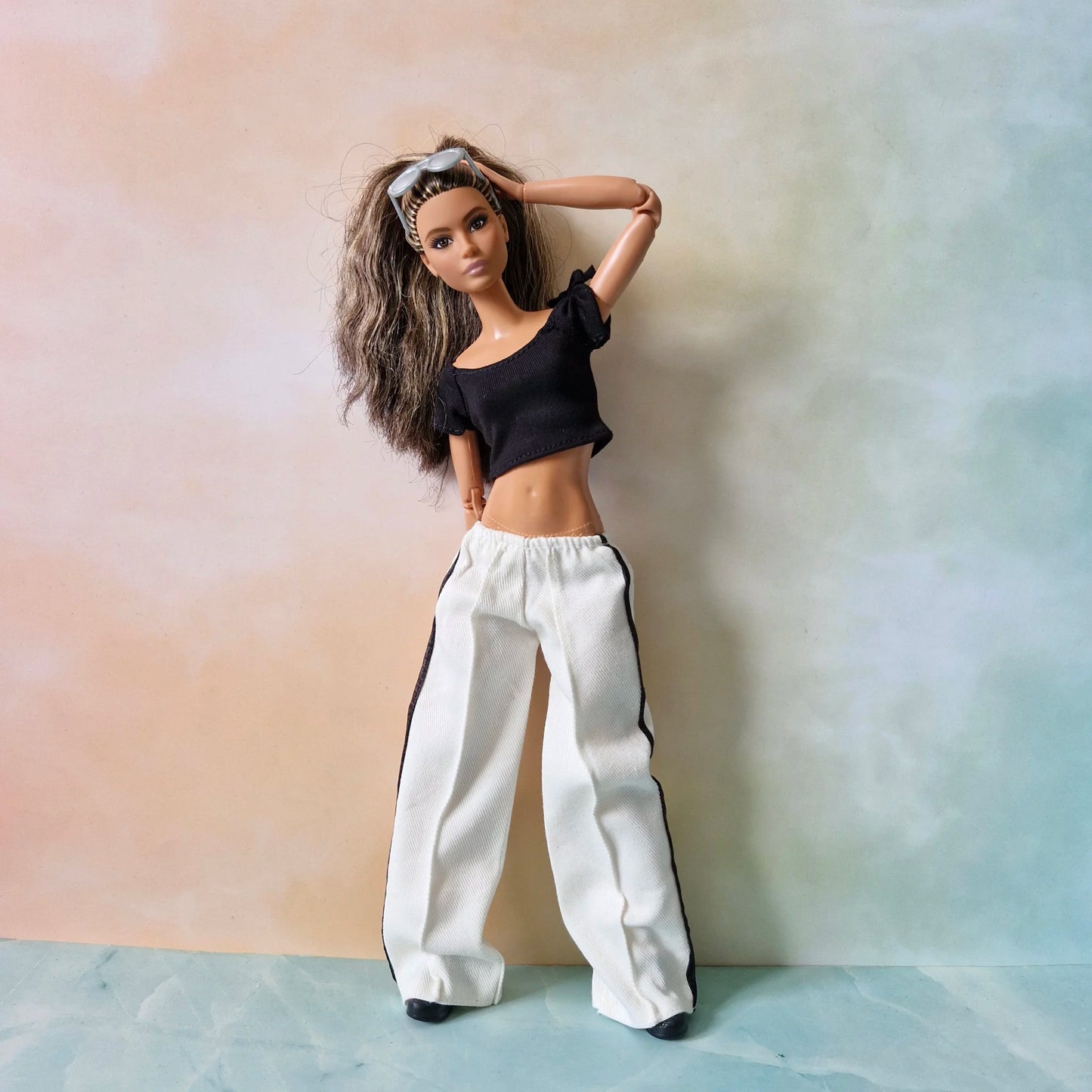 Barbie doll models black crop top and white striped pants outfit, hand on head pose.