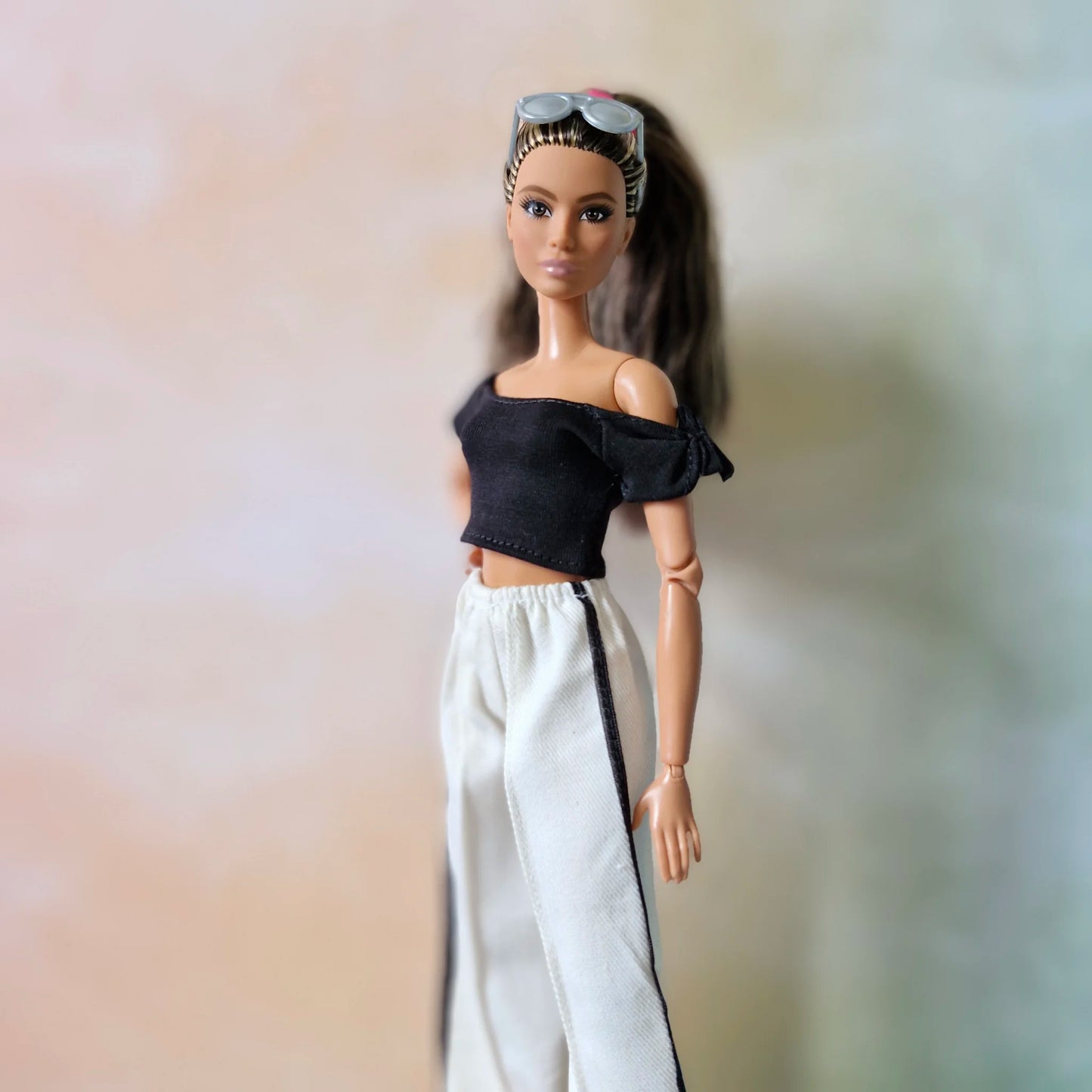 Barbie doll wearing casual black crop top, white striped pants, and sunglasses on head.