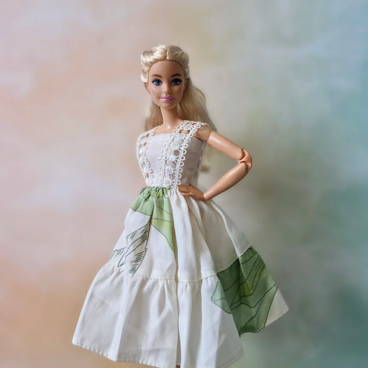 White sleeveless Barbie doll summer dress featuring green tropical leaf print and lace bodice overlay.