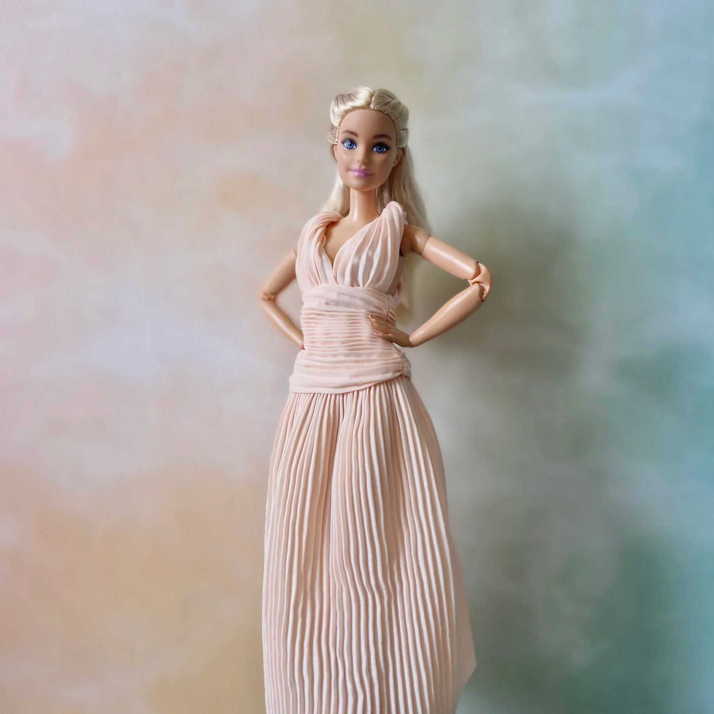 Blonde Barbie doll with hands on hips wearing sleeveless blush pink pleated gown with deep V-neck ruched bodice.