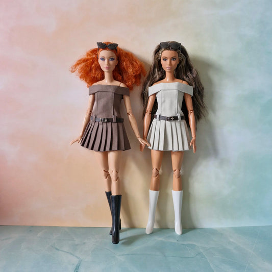 Two Barbie dolls side-by-side wearing matching off-shoulder pleated dresses in brown and grey