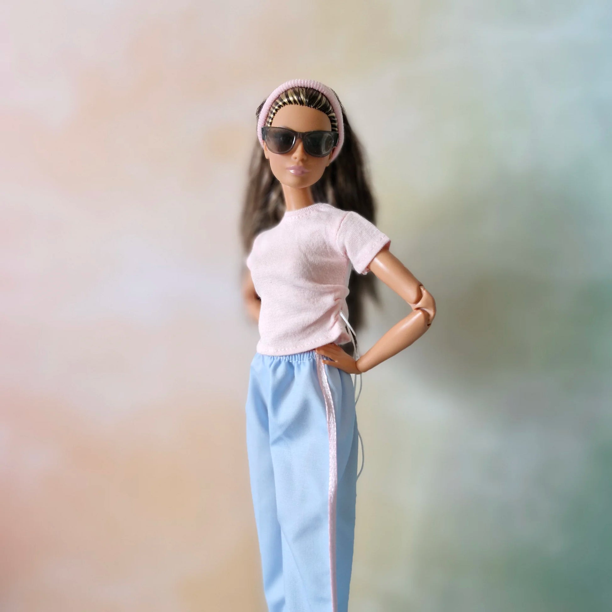 Close-up of Barbie doll wearing sunglasses, pink headband, pink drawstring top, and blue wide-leg pants.