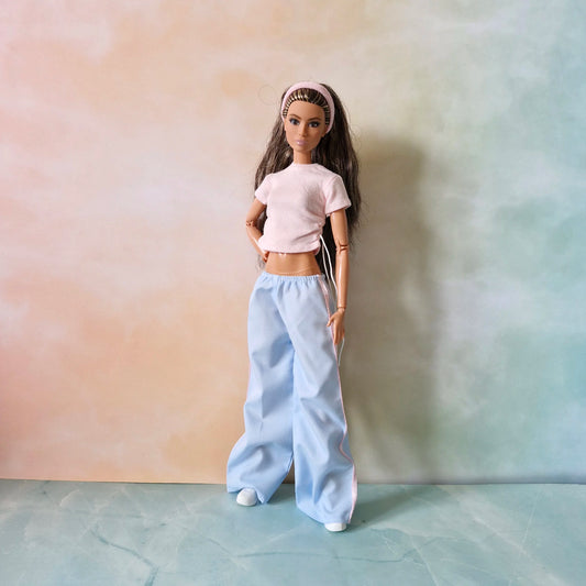 Brunette Barbie doll wearing pink textured drawstring top, light blue wide-leg pants with pink stripe, and pink headband.