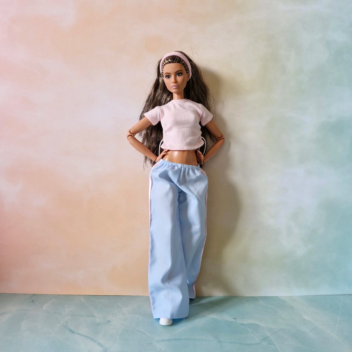 Full view of brunette Barbie doll wearing trendy outfit: pink drawstring tee, blue wide-leg pants, and pink headband.