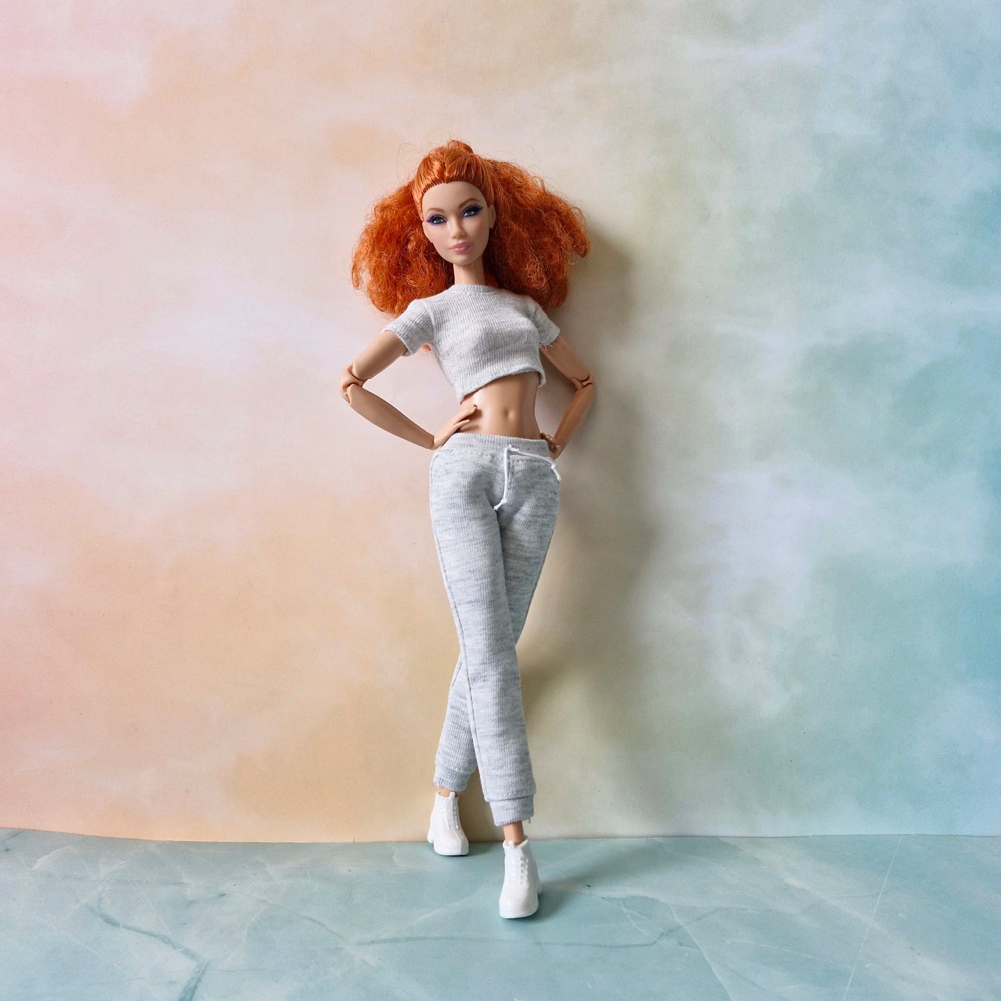 Redhead Barbie doll in full loungewear outfit: grey knit crop top, joggers, and white sneakers, posing with crossed legs.