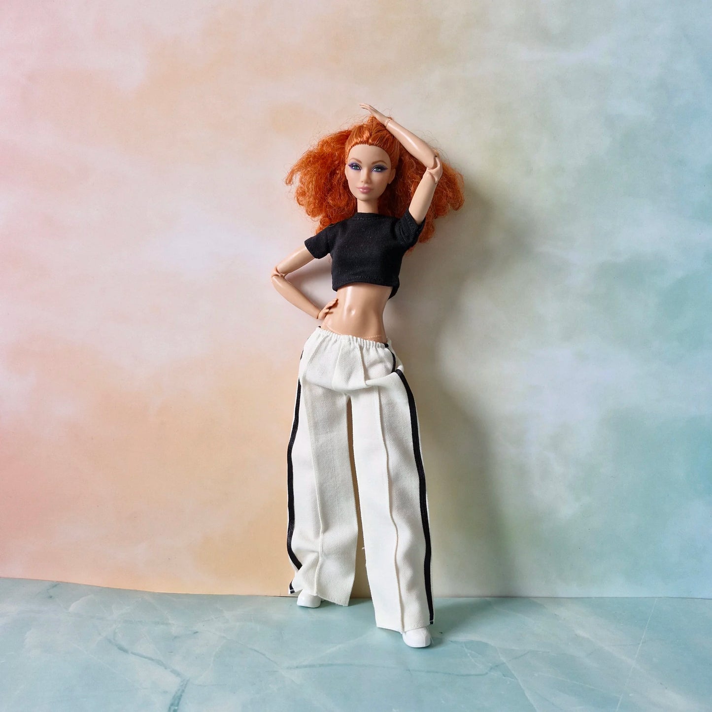 Red-haired Barbie doll wearing black crop top and white wide-leg striped pants set.