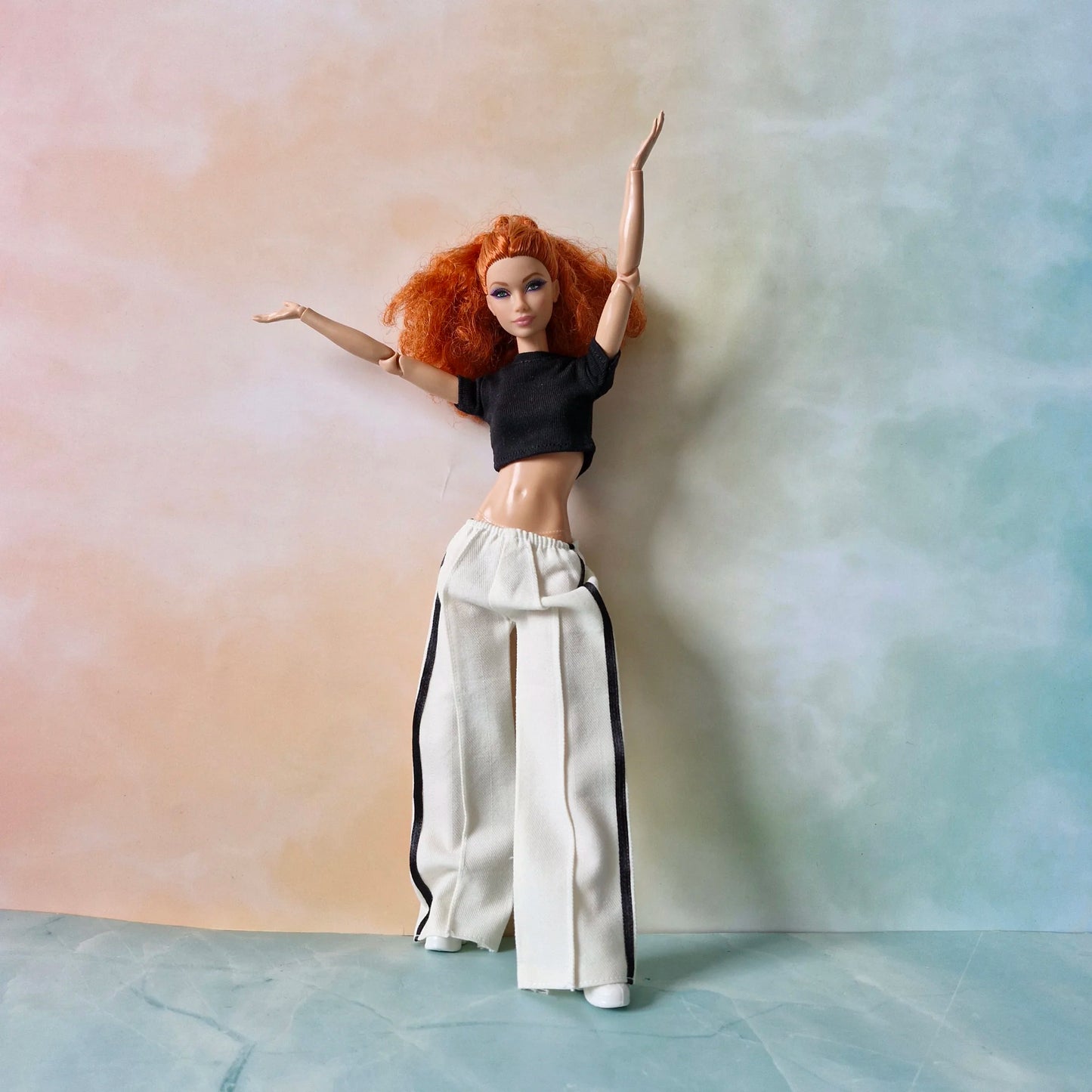 Dynamic pose of red-haired Barbie in black crop top and white striped pants outfit.