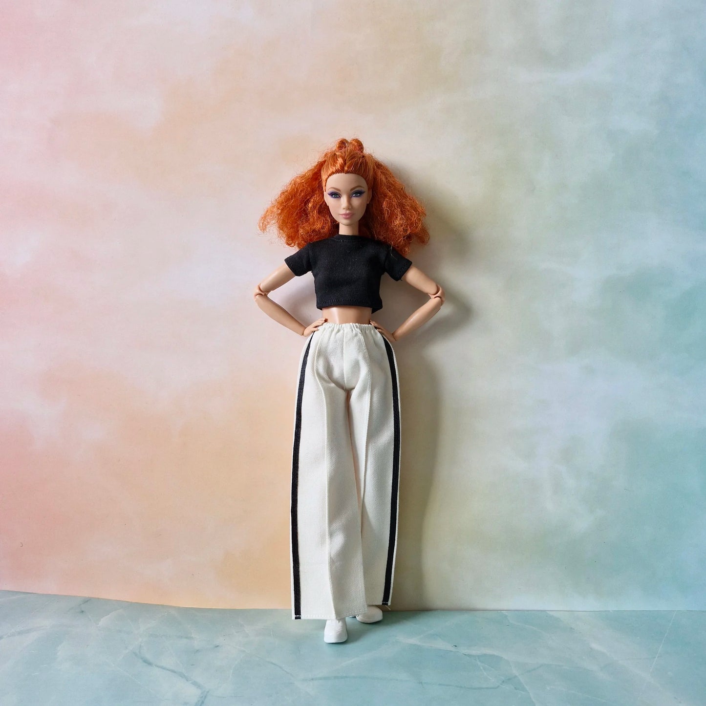 Front view of red-haired Barbie doll modeling black crop top and white striped pants.