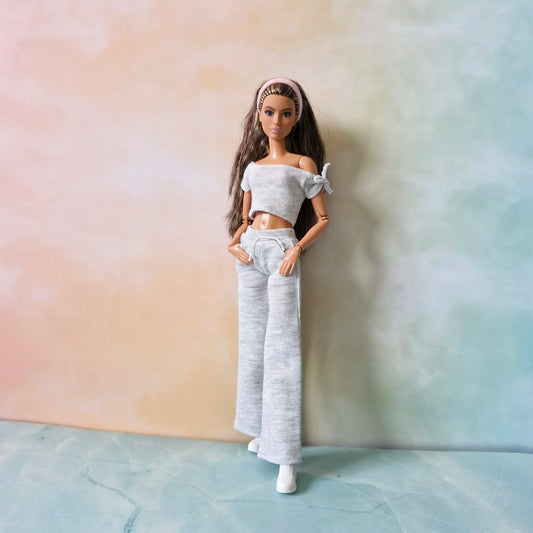 BruneBrunette Barbie doll wearing grey knit off-shoulder crop top with tie detail and matching wide-leg lounge pants.tte Barbie doll wearing grey knit off-shoulder crop top with tie detail and matching wide-leg lounge pants.