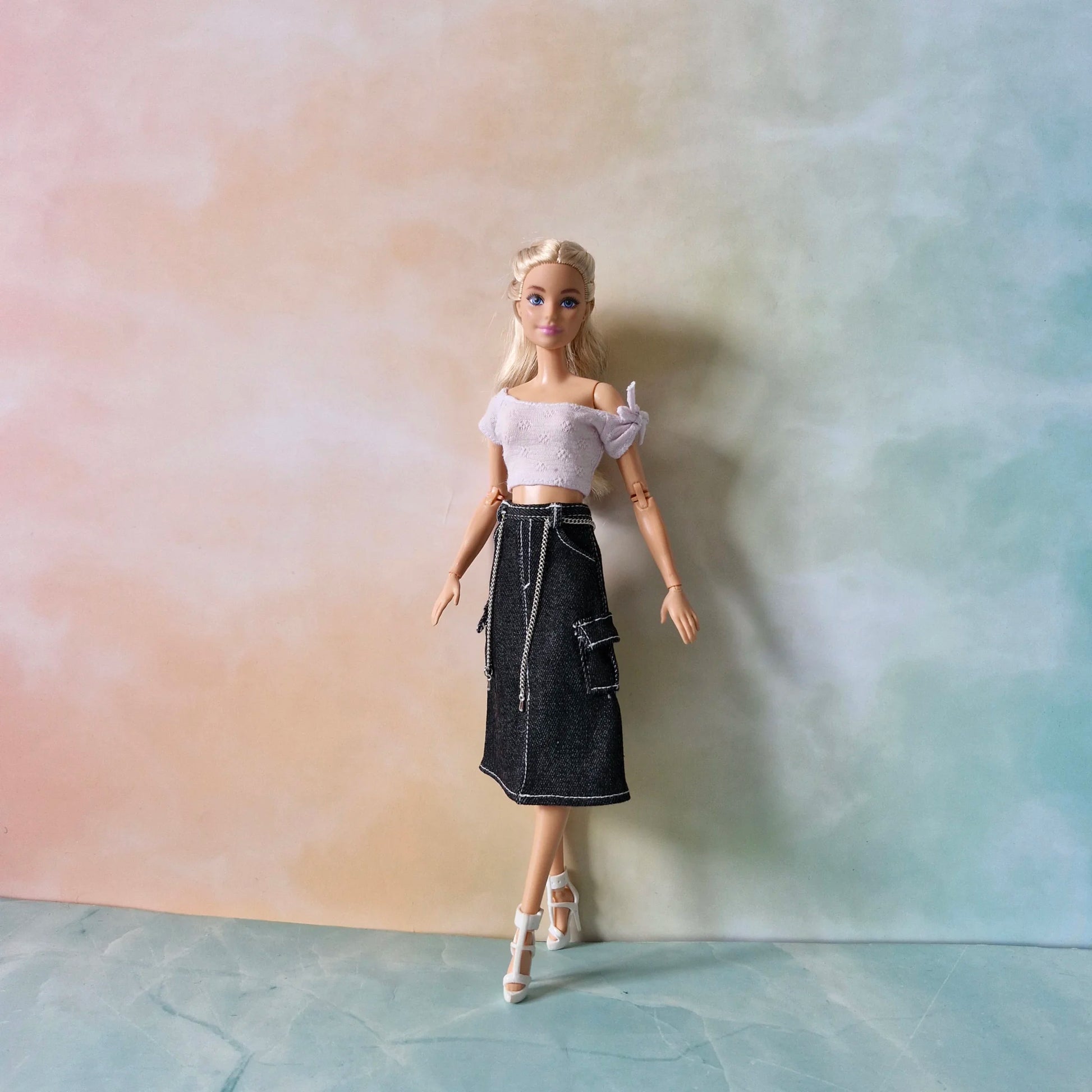 Full view of Barbie doll in trendy outfit: lavender crop top, dark denim midi cargo skirt with chain, white heels.