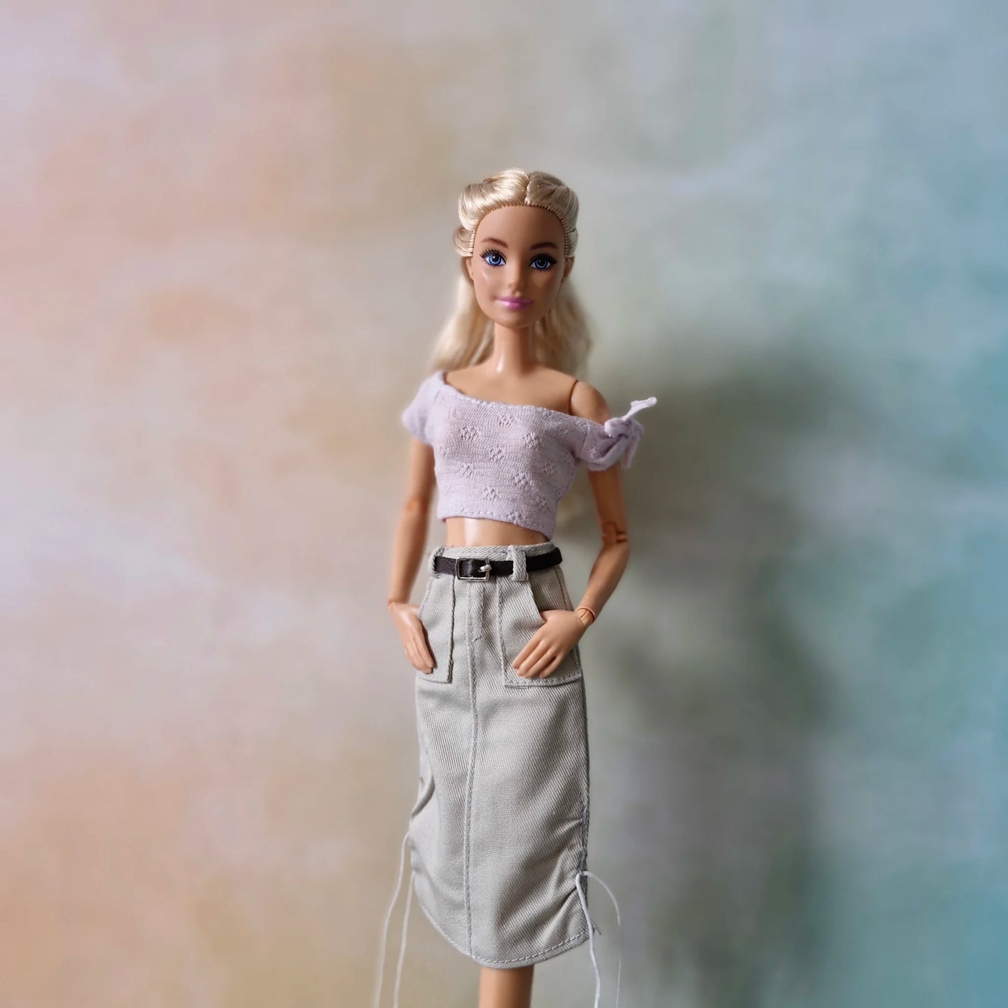 Barbie doll poses in lavender crop top and grey belted midi skirt with front pockets and drawstrings.