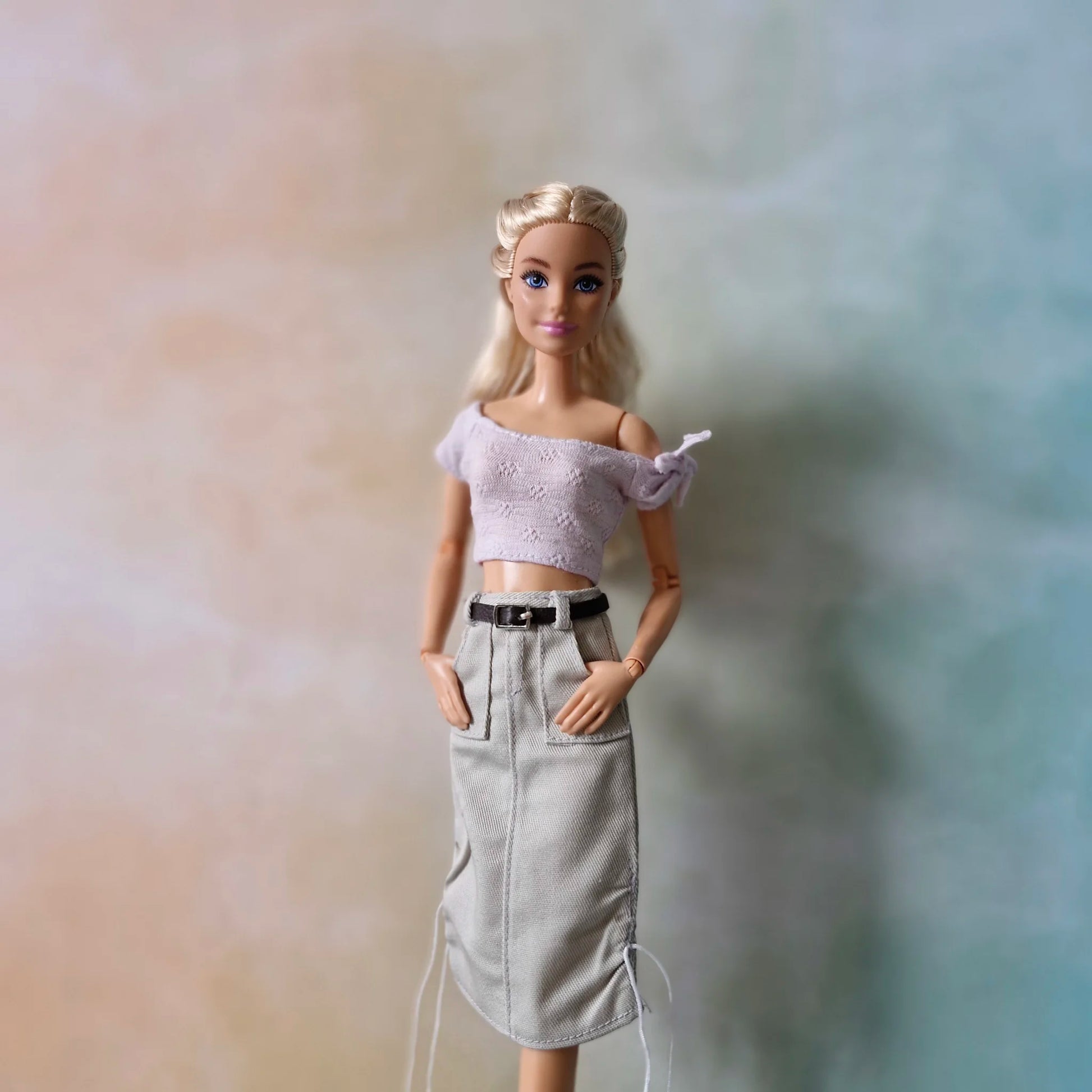 Barbie doll poses in lavender crop top and grey belted midi skirt with front pockets and drawstrings.
