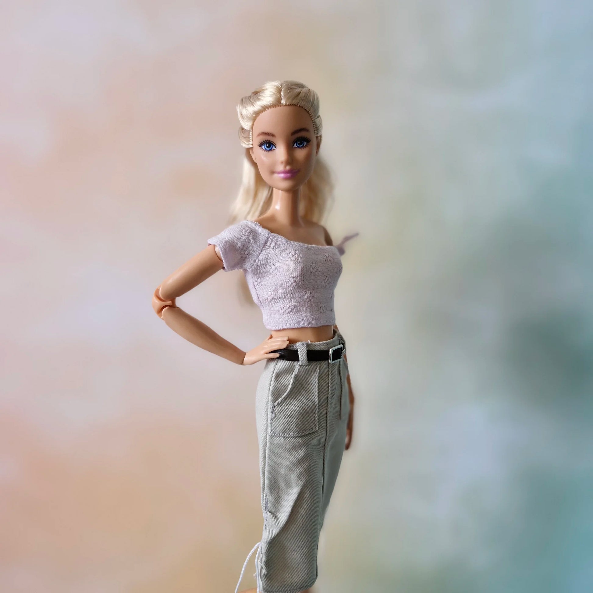 Side view of Barbie fashion doll in chic outfit: lavender off-shoulder top, grey belted utility skirt.
