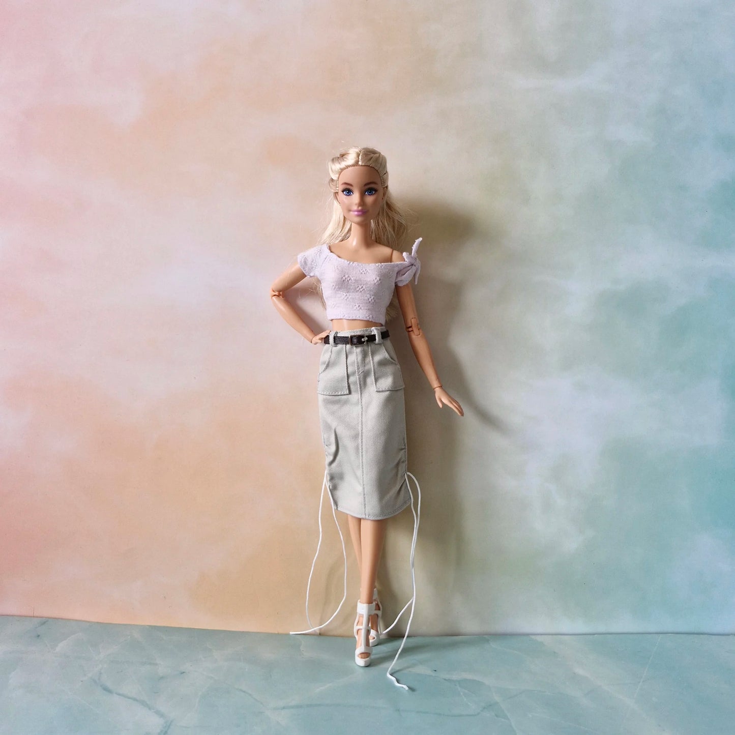 Full view of Barbie doll wearing versatile fashion pack: lavender top, grey utility midi skirt with belt, white heels.