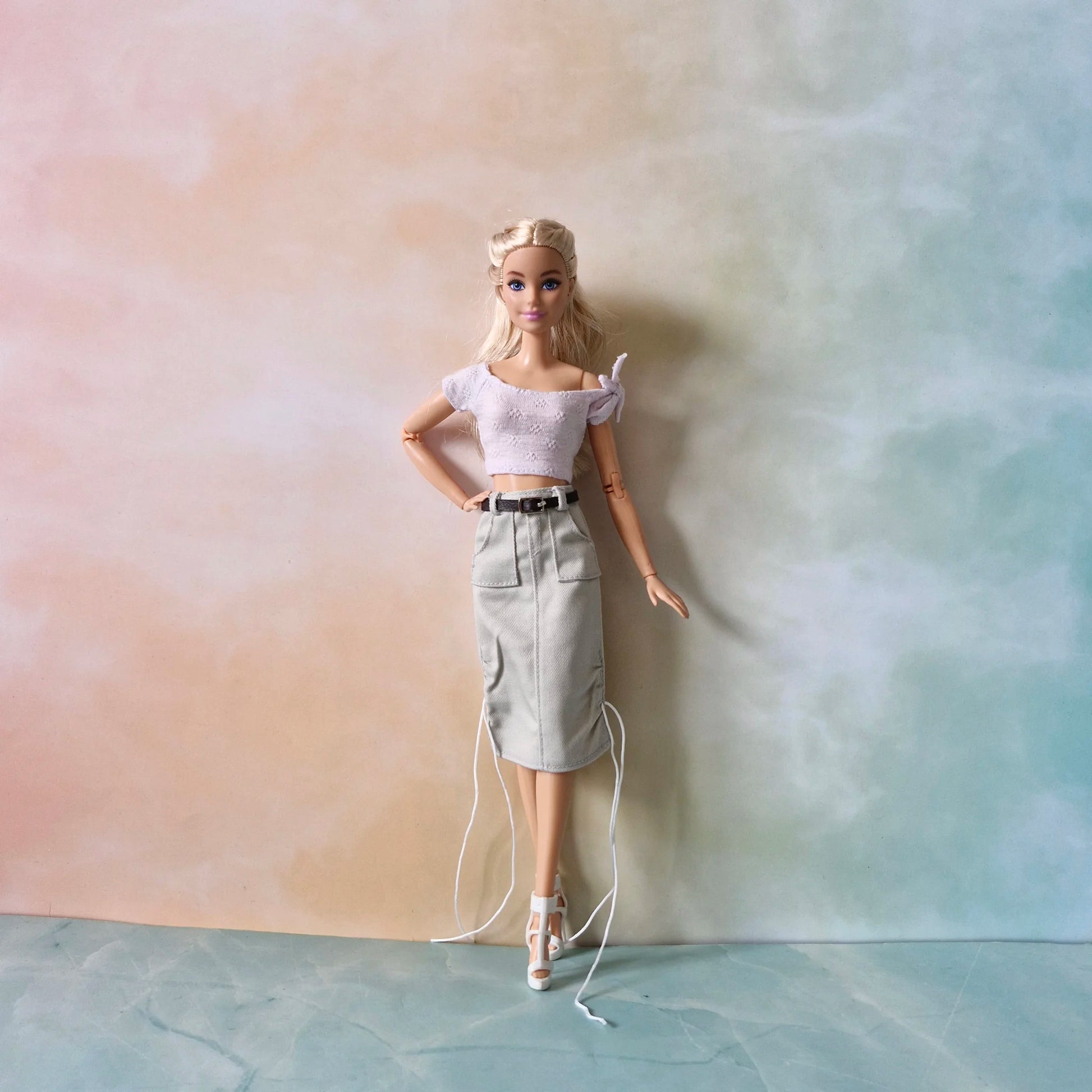 Full view of Barbie doll wearing versatile fashion pack: lavender top, grey utility midi skirt with belt, white heels.