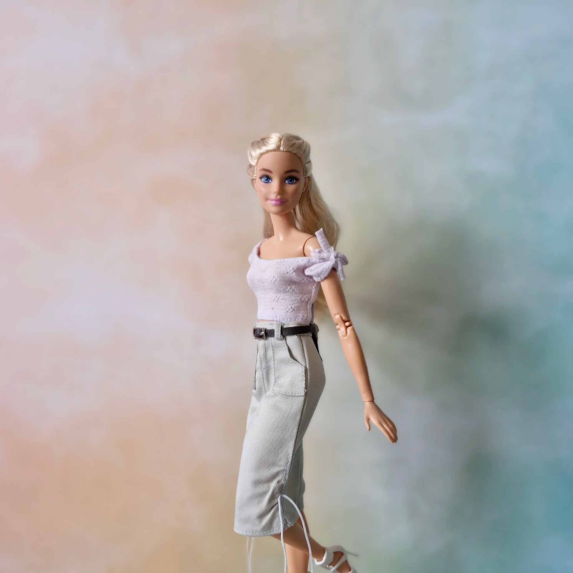 Blonde Barbie doll models stylish set: lavender tie-shoulder top and light grey midi skirt with belt.