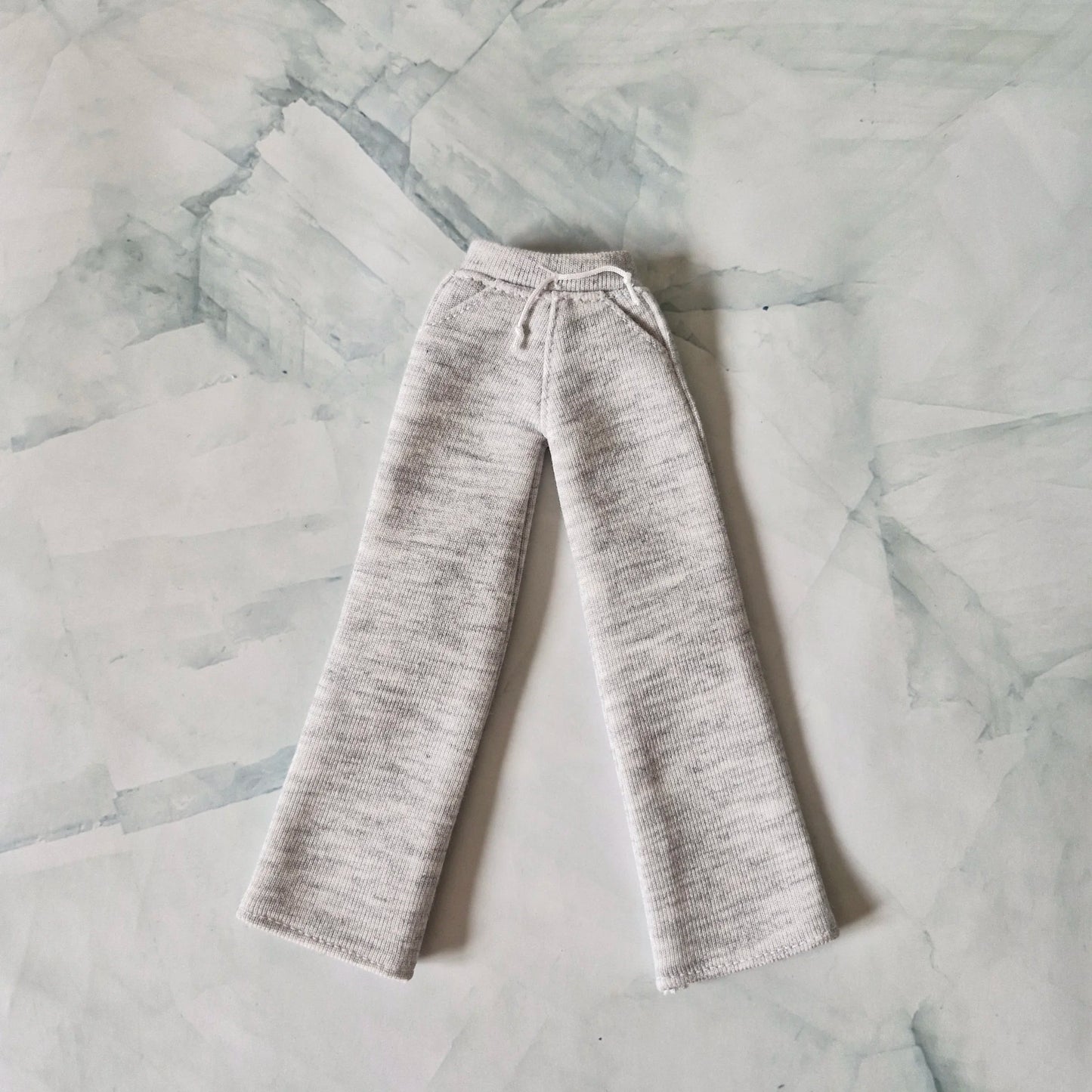 Light grey heather knit wide-leg lounge pantsLight grey heather knit wide-leg lounge pants for Barbie doll with drawstring waist detail, laid flat on marble background. for Barbie doll with drawstring waist detail, laid flat on marble background.