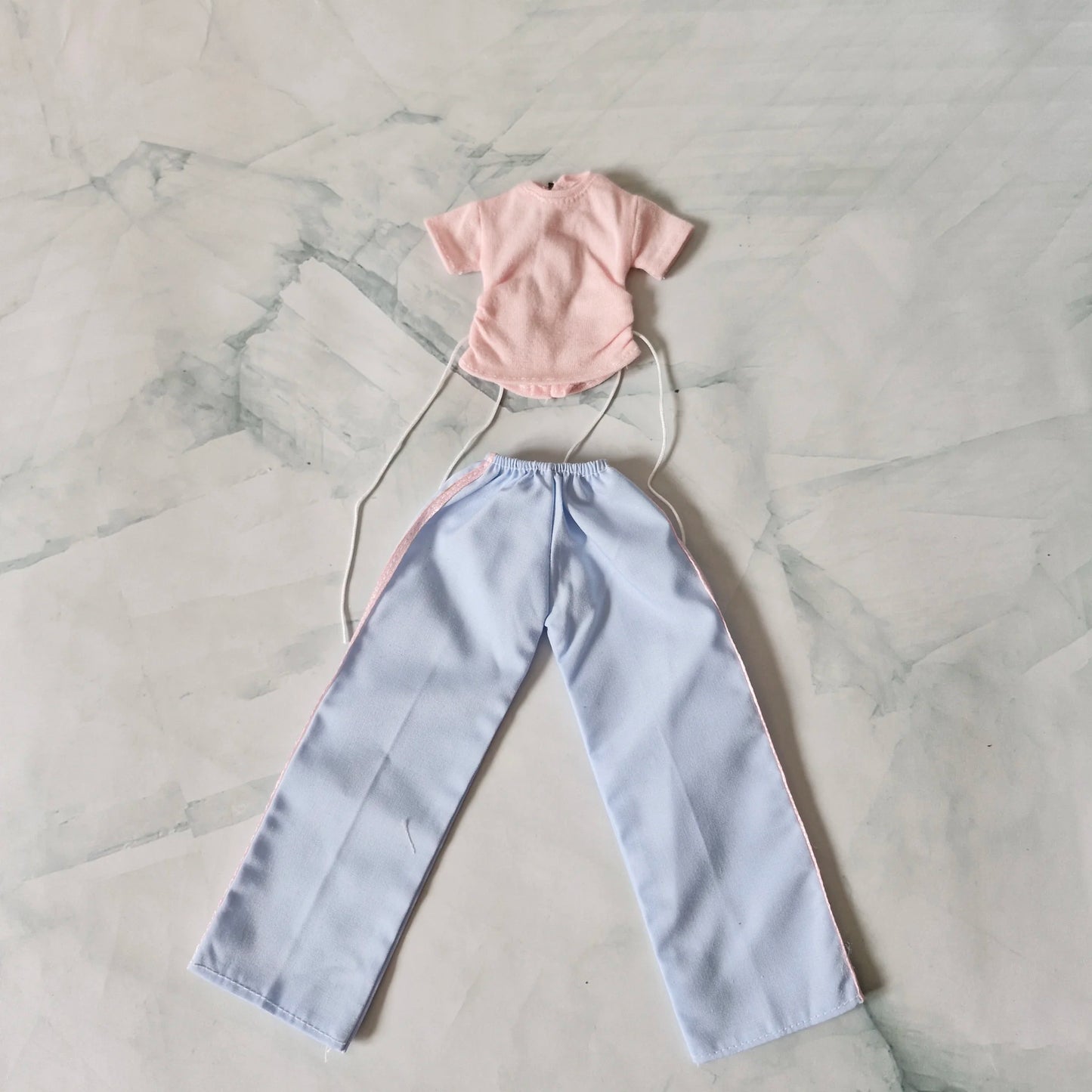 Barbie doll outfit set laid flat: pale pink drawstring t-shirt and light blue wide-leg pants with pink stripes.