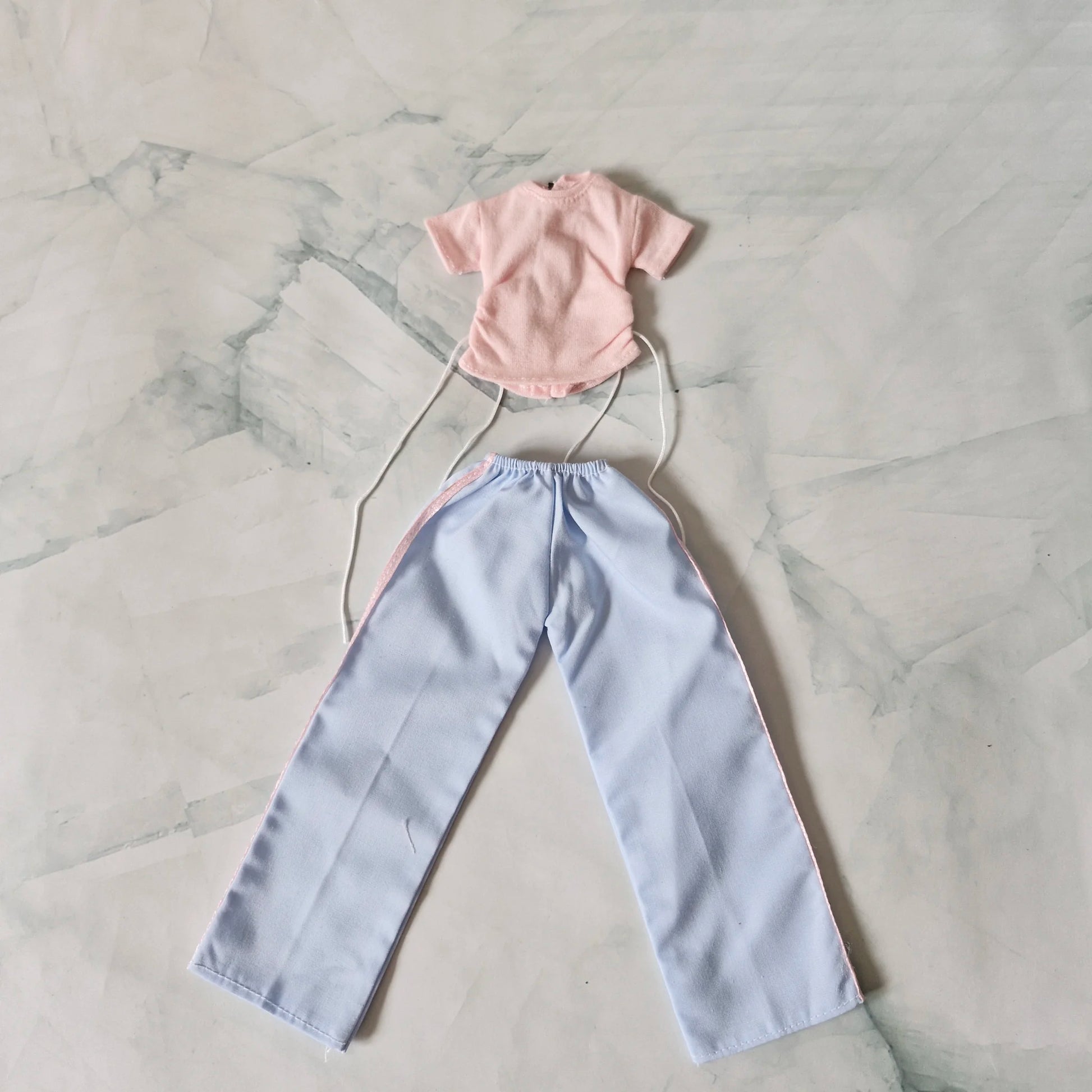 Barbie doll outfit set laid flat: pale pink drawstring t-shirt and light blue wide-leg pants with pink stripes.