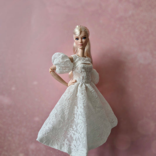 Blonde Barbie wearing white lace puff sleeve dress against a soft pink background.