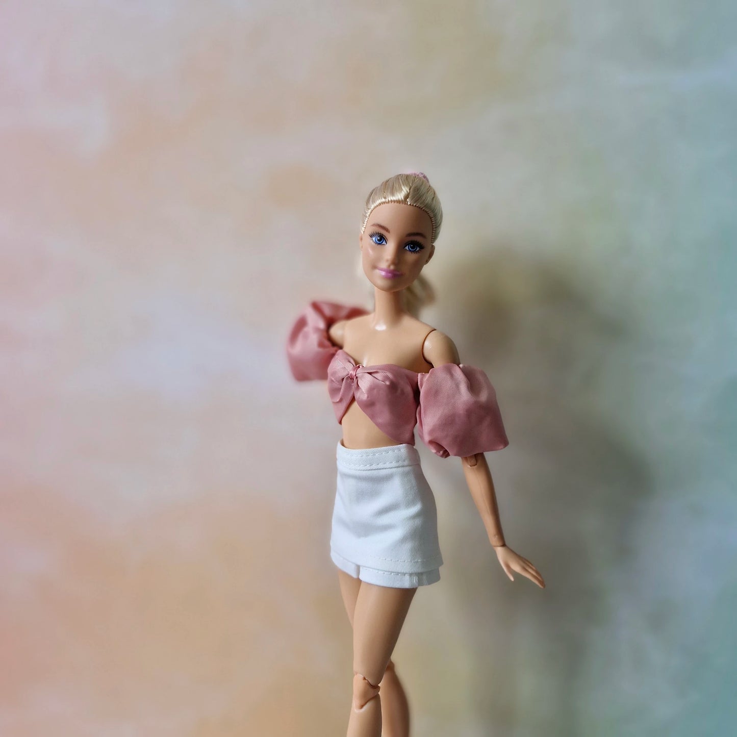 Blonde Barbie doll models dusty rose off-shoulder puff sleeve top with bow and white mini skirt.
