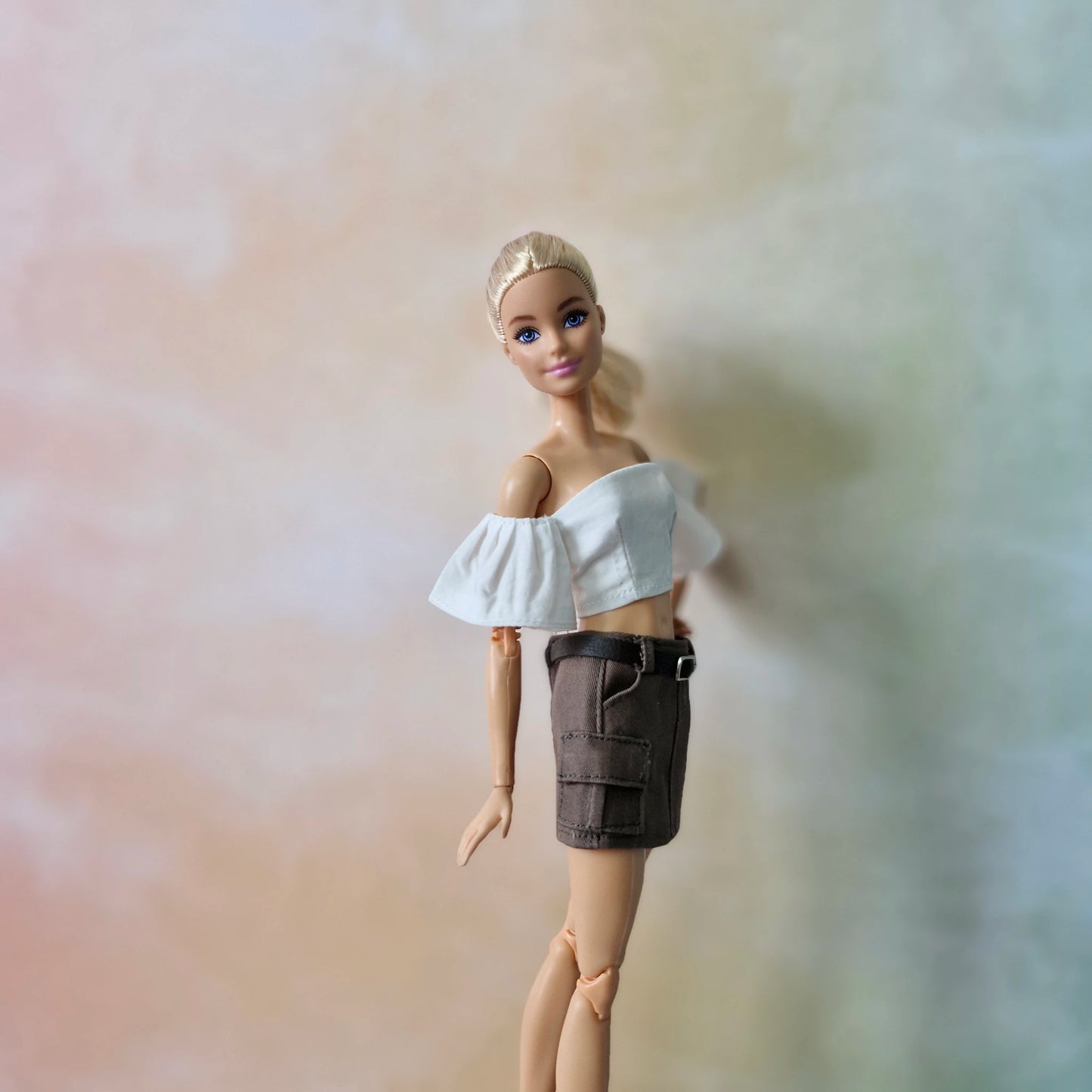 Close-up of blonde Barbie wearing white off-shoulder top and brown utility mini skirt.