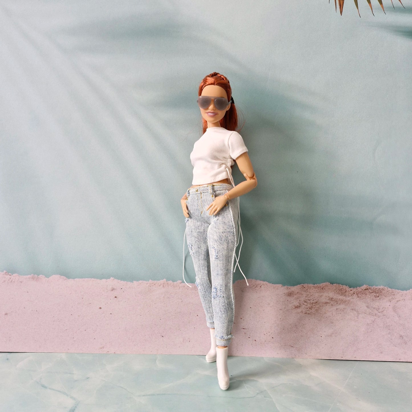 Barbie doll wearing a white top and patterned pants with sunglasses against a plain background