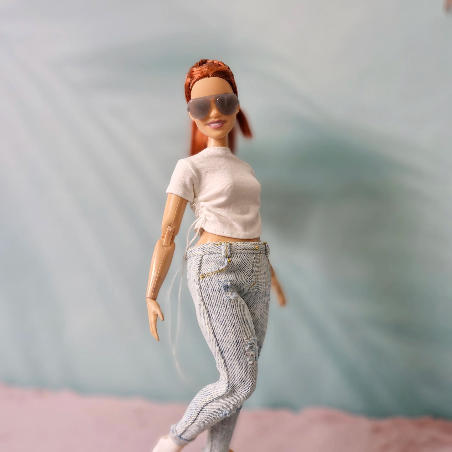 Curvy Barbie doll in a dynamic pose showing off the side-tie detail on her white t-shirt and the fit of the distressed jeans.