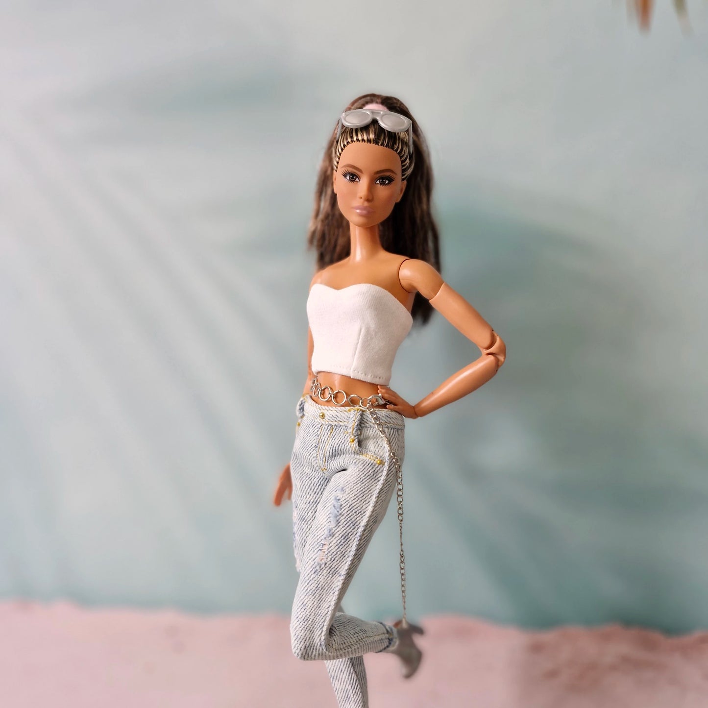 Brunette Barbie doll posing on one leg, wearing a white tube top, distressed jeans with chain, and silver boots.