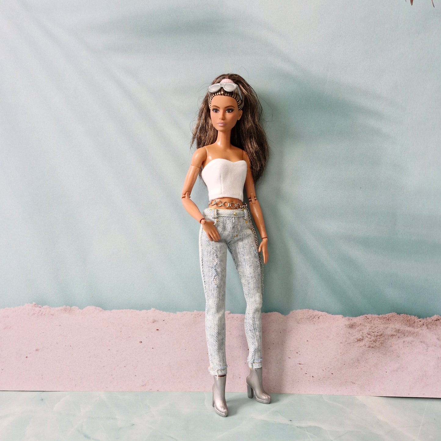 Full-length view of a brunette Barbie doll in a white tube top, distressed jeans, and silver boots, standing confidently.