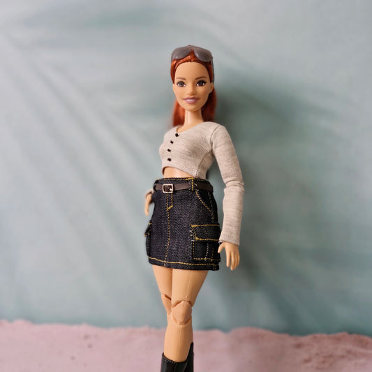 Red-haired Barbie doll wearing a 3-piece outfit: denim cargo skirt, grey long-sleeve crop top, and black boots.
