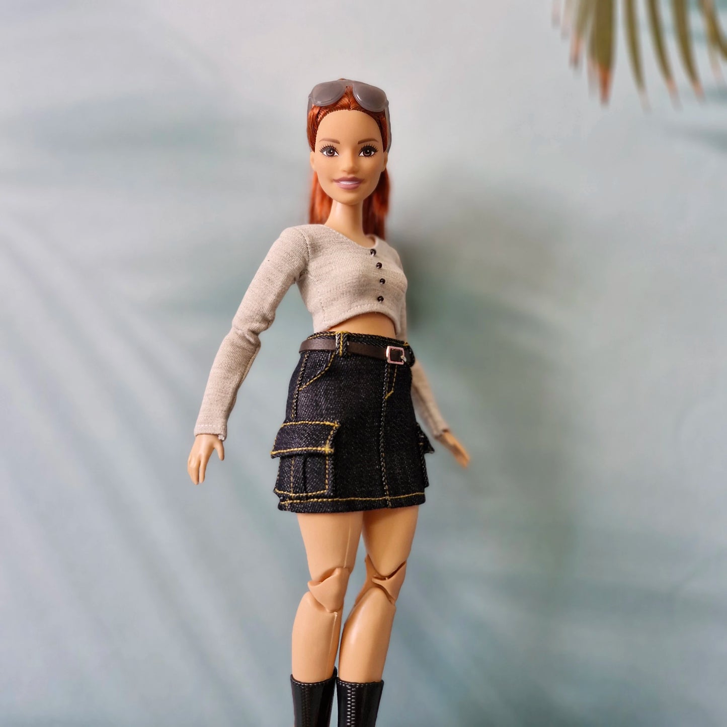 Close-up of a Barbie doll modeling a modern outfit set featuring a dark denim cargo skirt and a grey top.