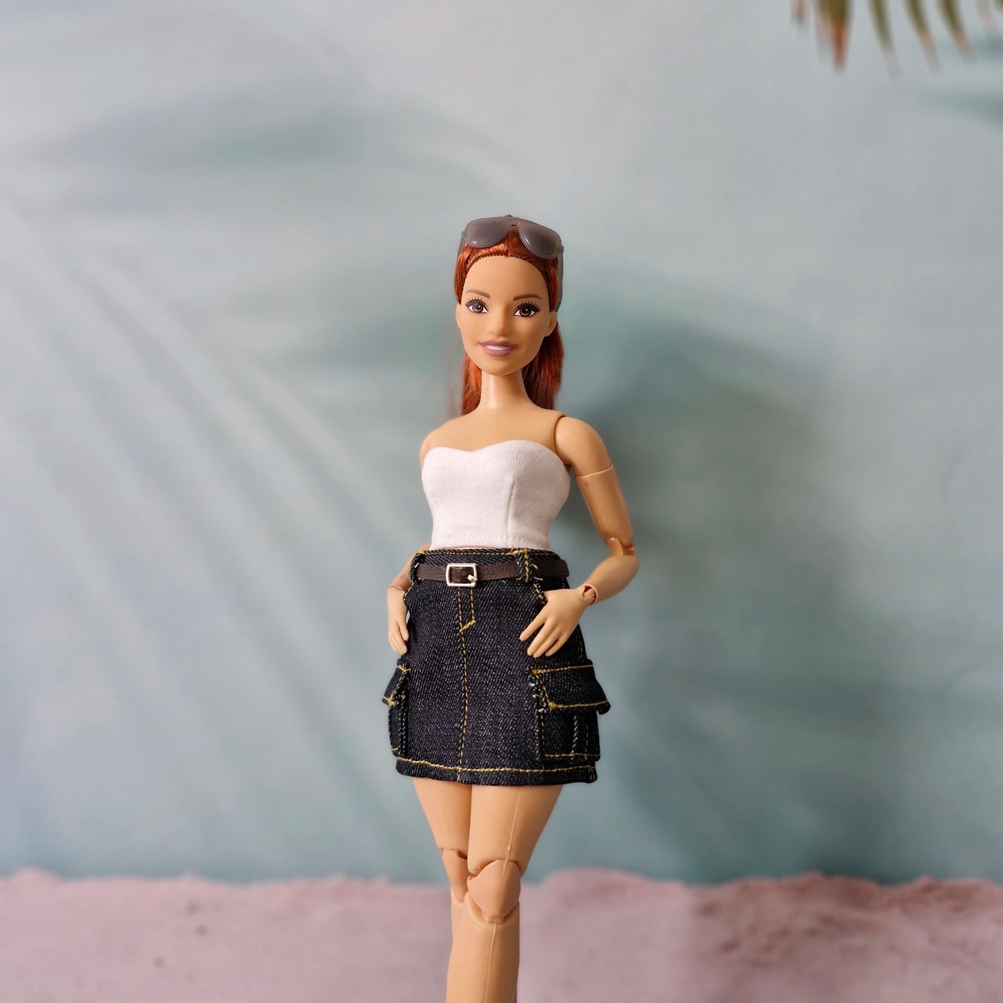 Barbie doll wearing a white top and denim skirt with sunglasses on head against a blurred background