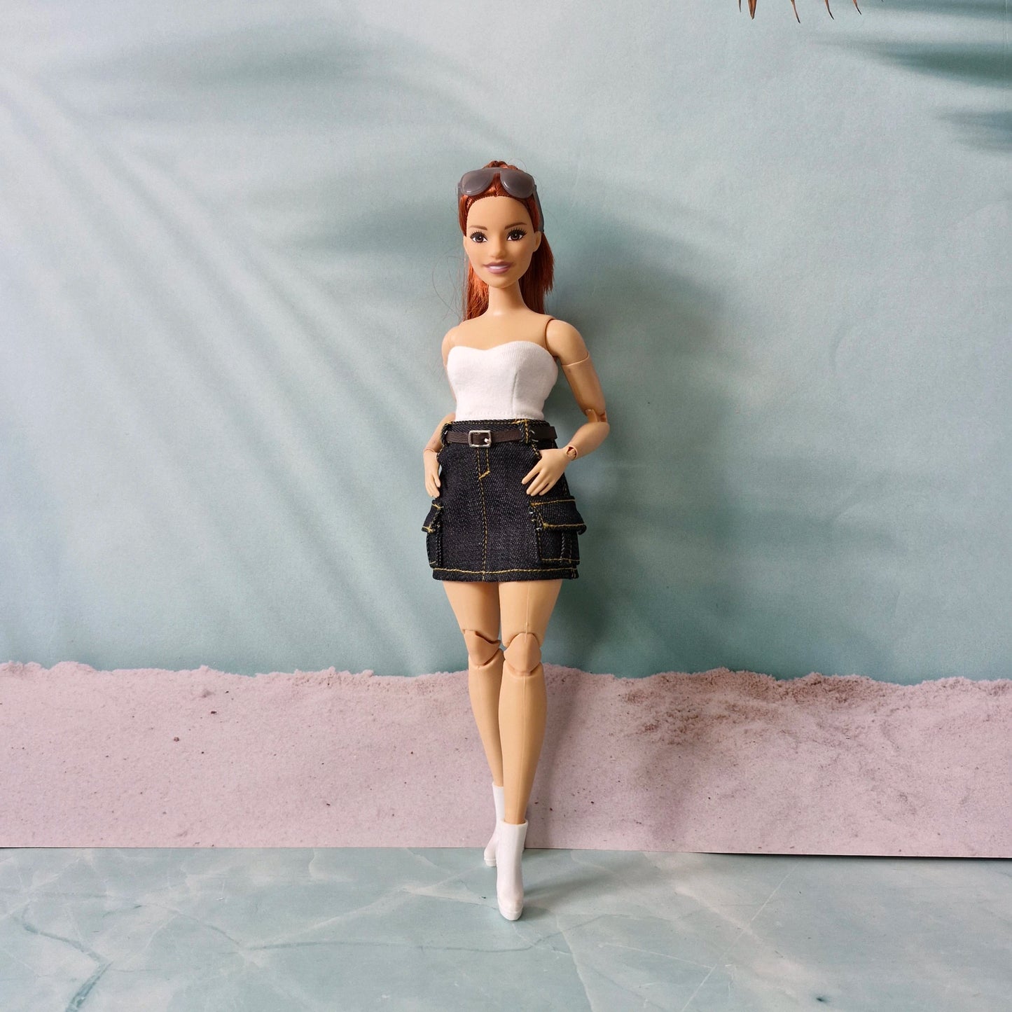 Barbie doll wearing a white top and denim skirt with a gray background