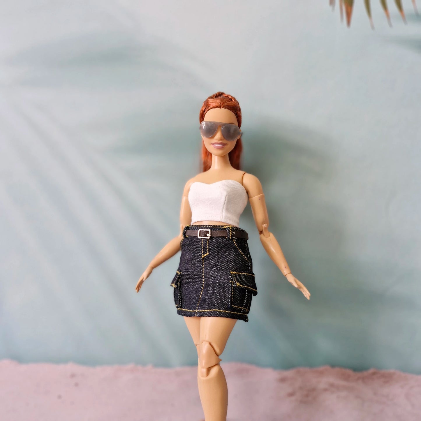 Barbie doll wearing sunglasses and a denim skirt on a neutral background