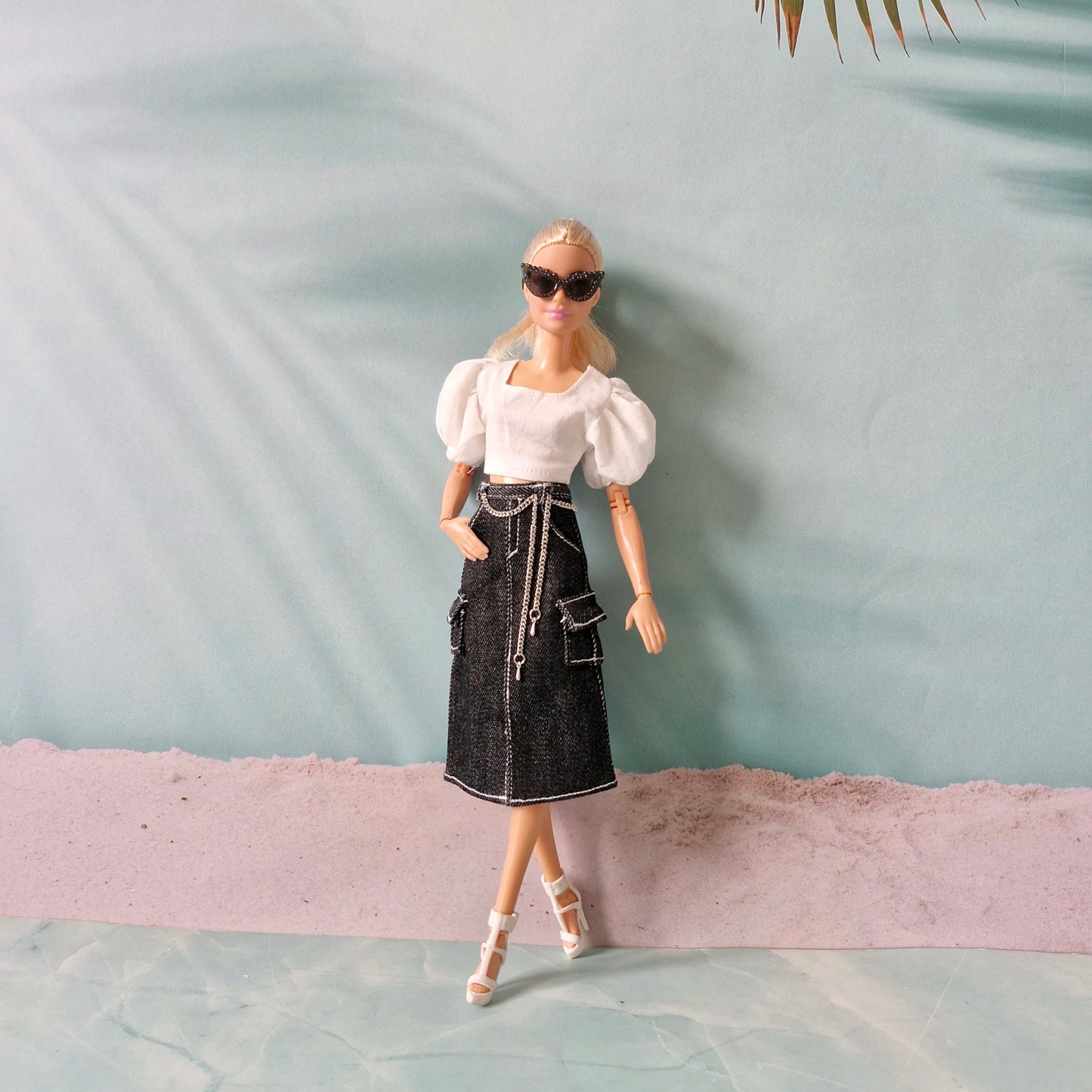 Barbie doll wearing a white top and black skirt with sunglasses against a light blue background