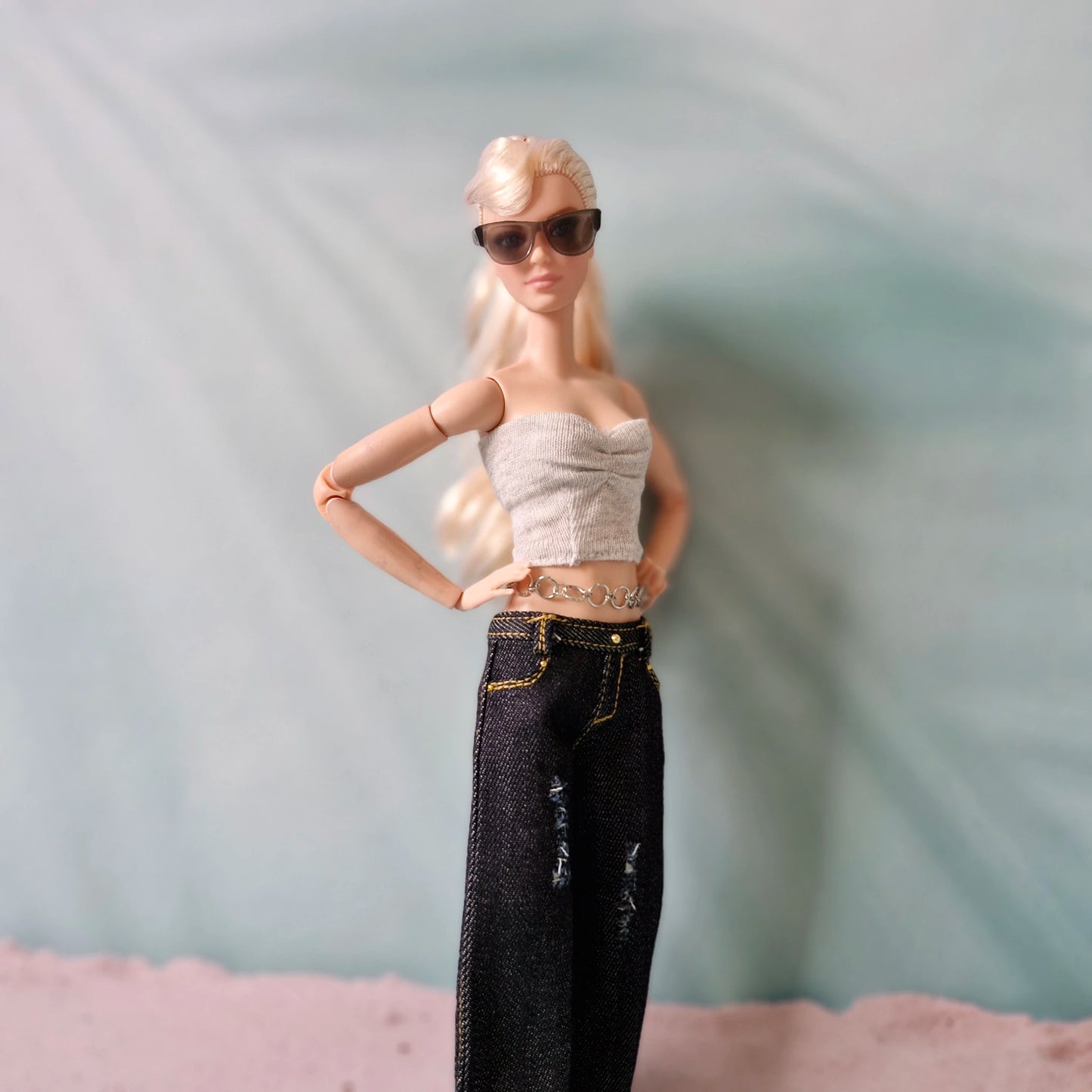 Barbie doll wearing sunglasses, a crop top, and high-waisted jeans against a neutral background