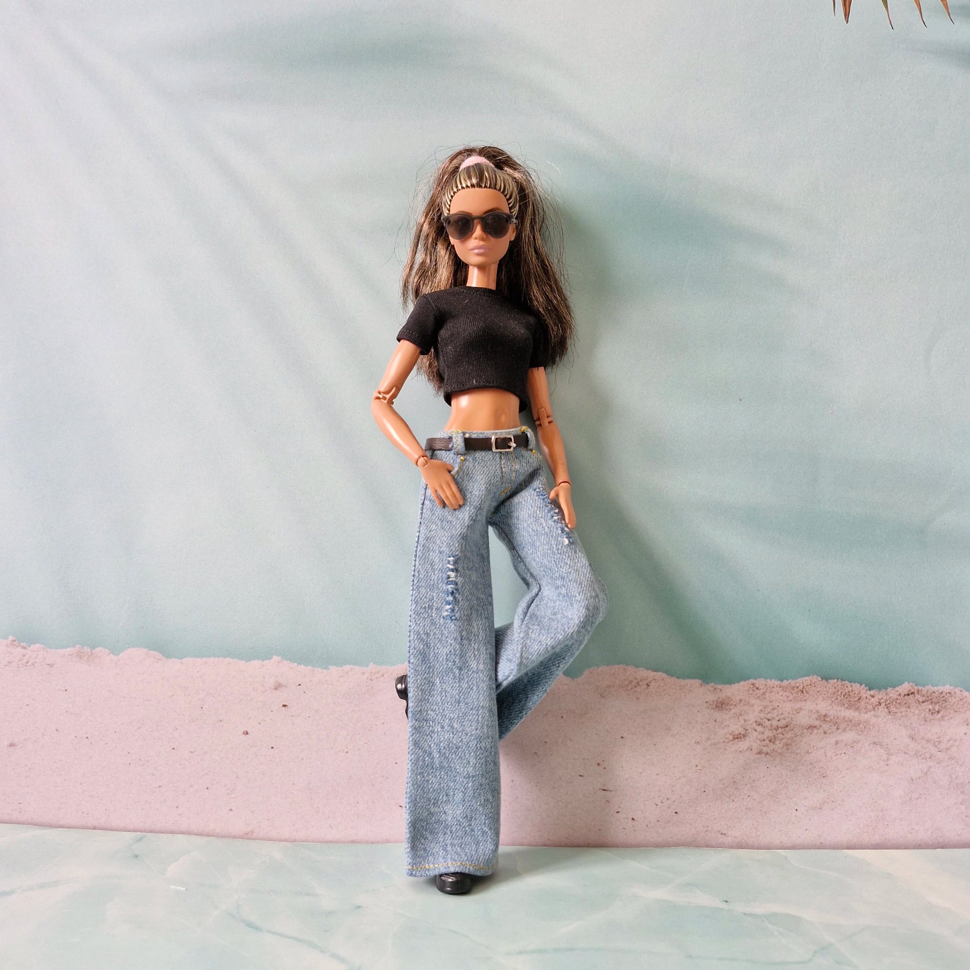 Barbie doll wearing a black top and gray jeans with sunglasses on a light green background